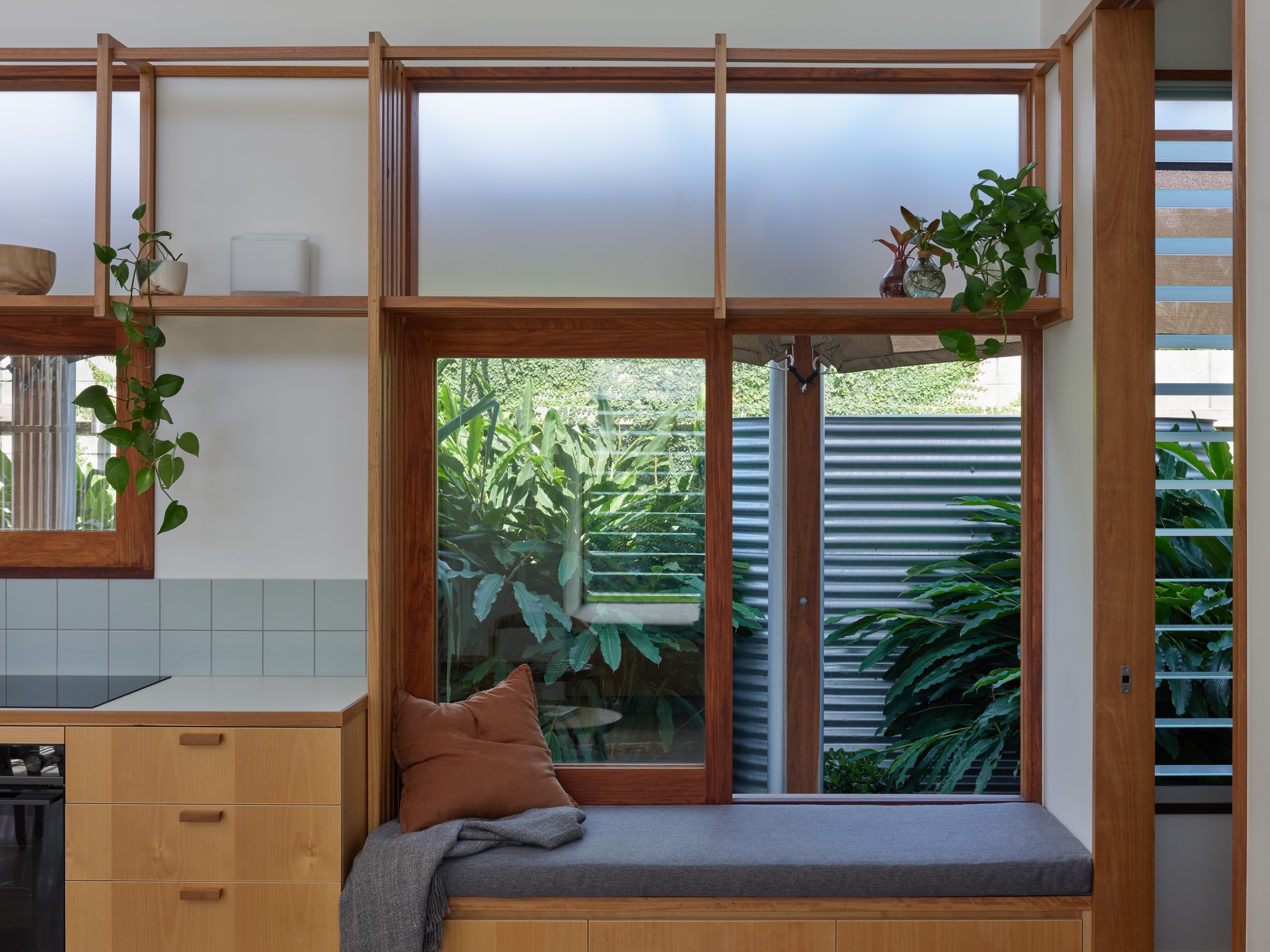 Built-in timber bench beneath clerestory windows overlooking a planted courtyard with corrugated metal fencing