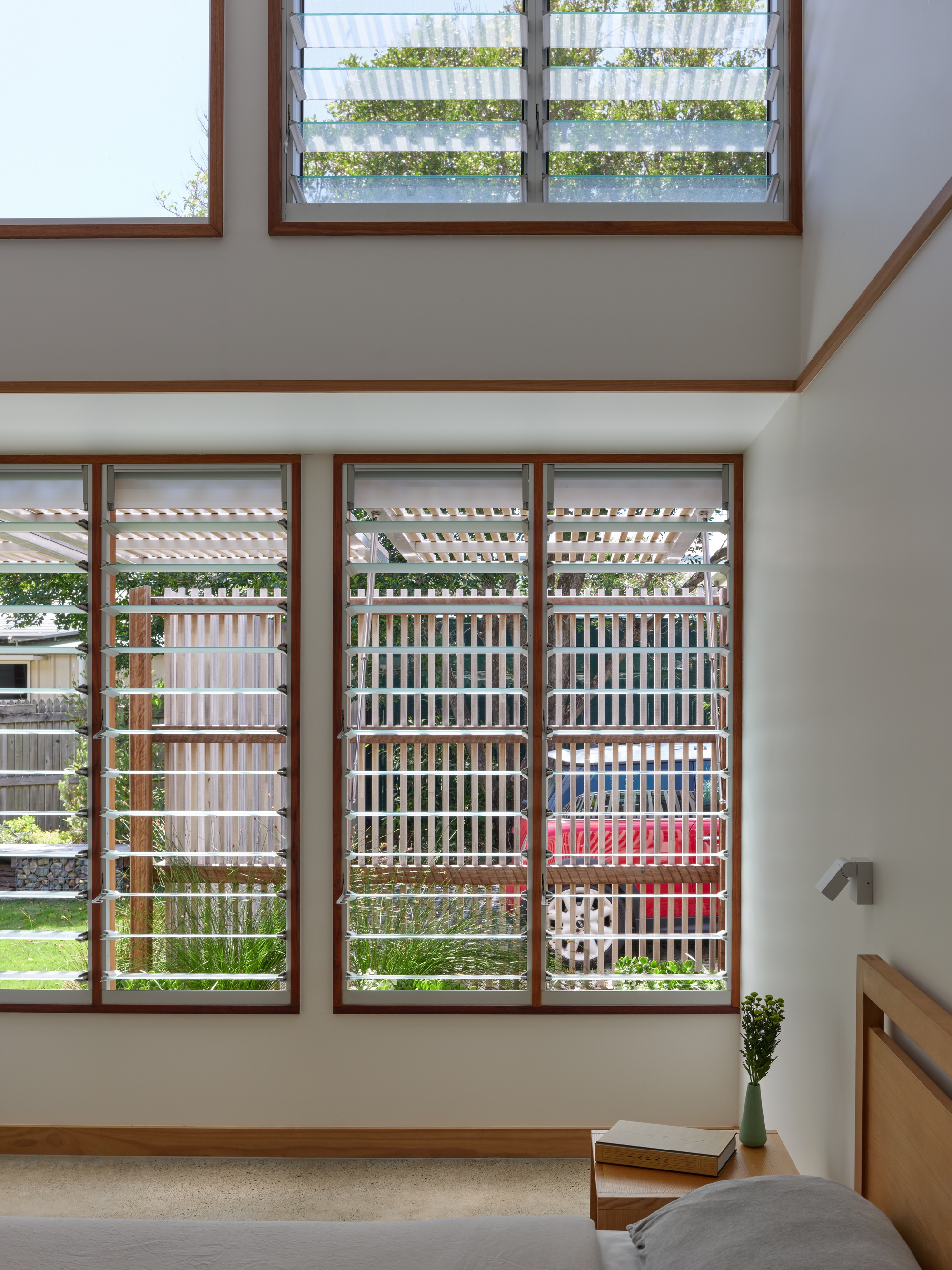 Double-height living space with timber-framed louvered windows filtering daylight into the interior