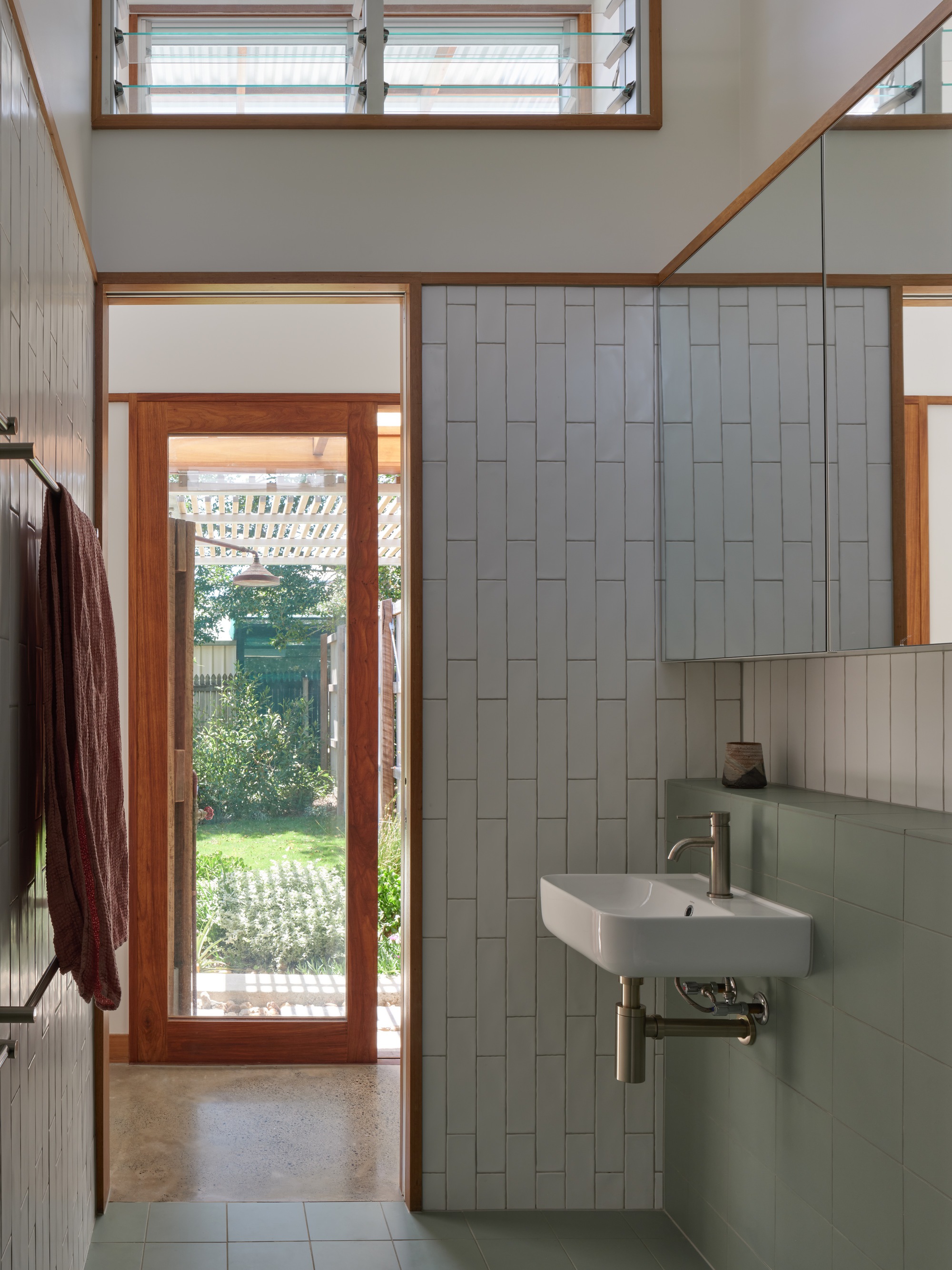 Entry hall with timber-framed glazed door opening to a garden and pale tiled wall beside a wall-mounted sink