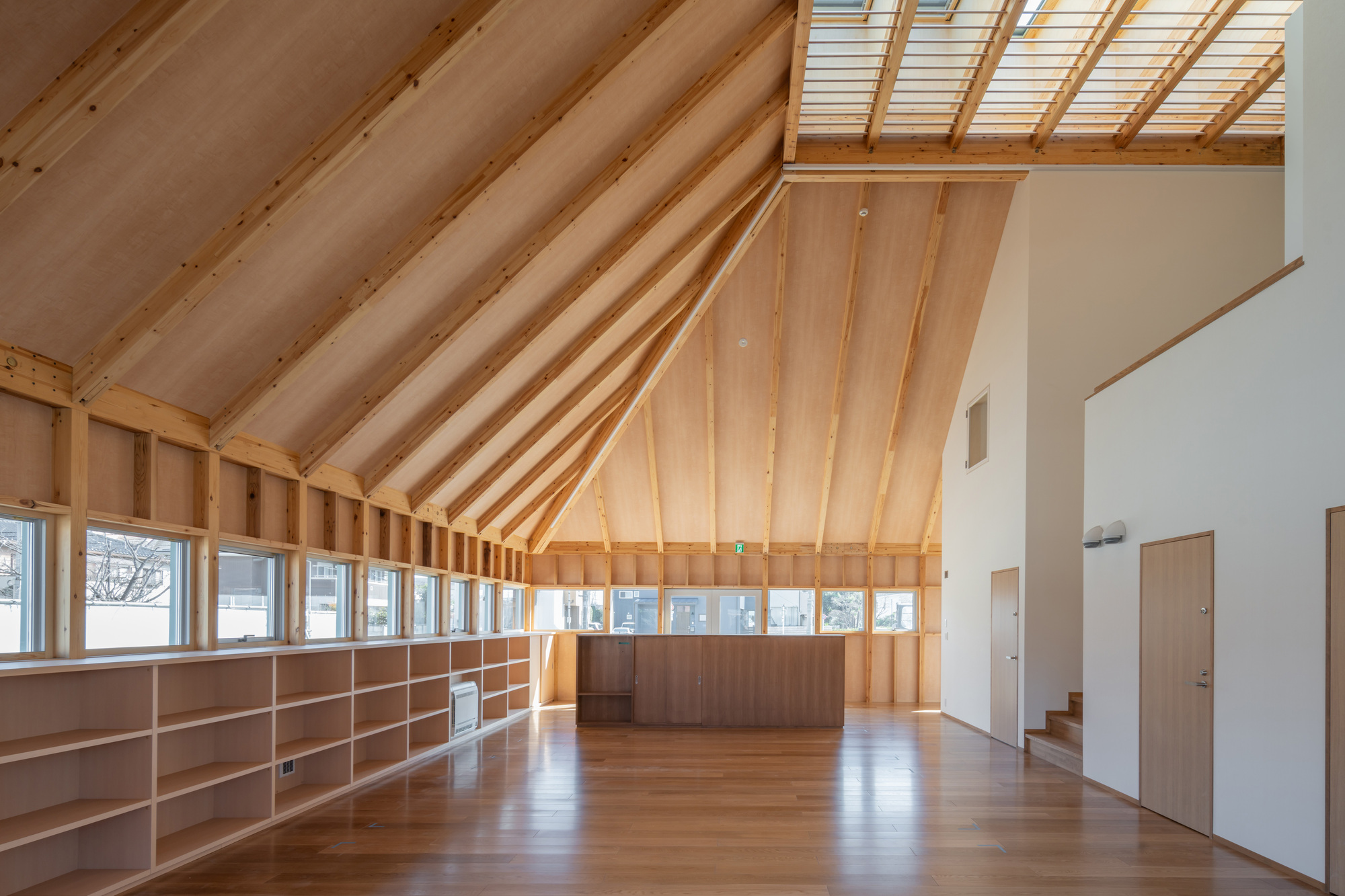 Interior space with exposed timber rafters, built-in plywood shelving along the walls, and a skylight overhead