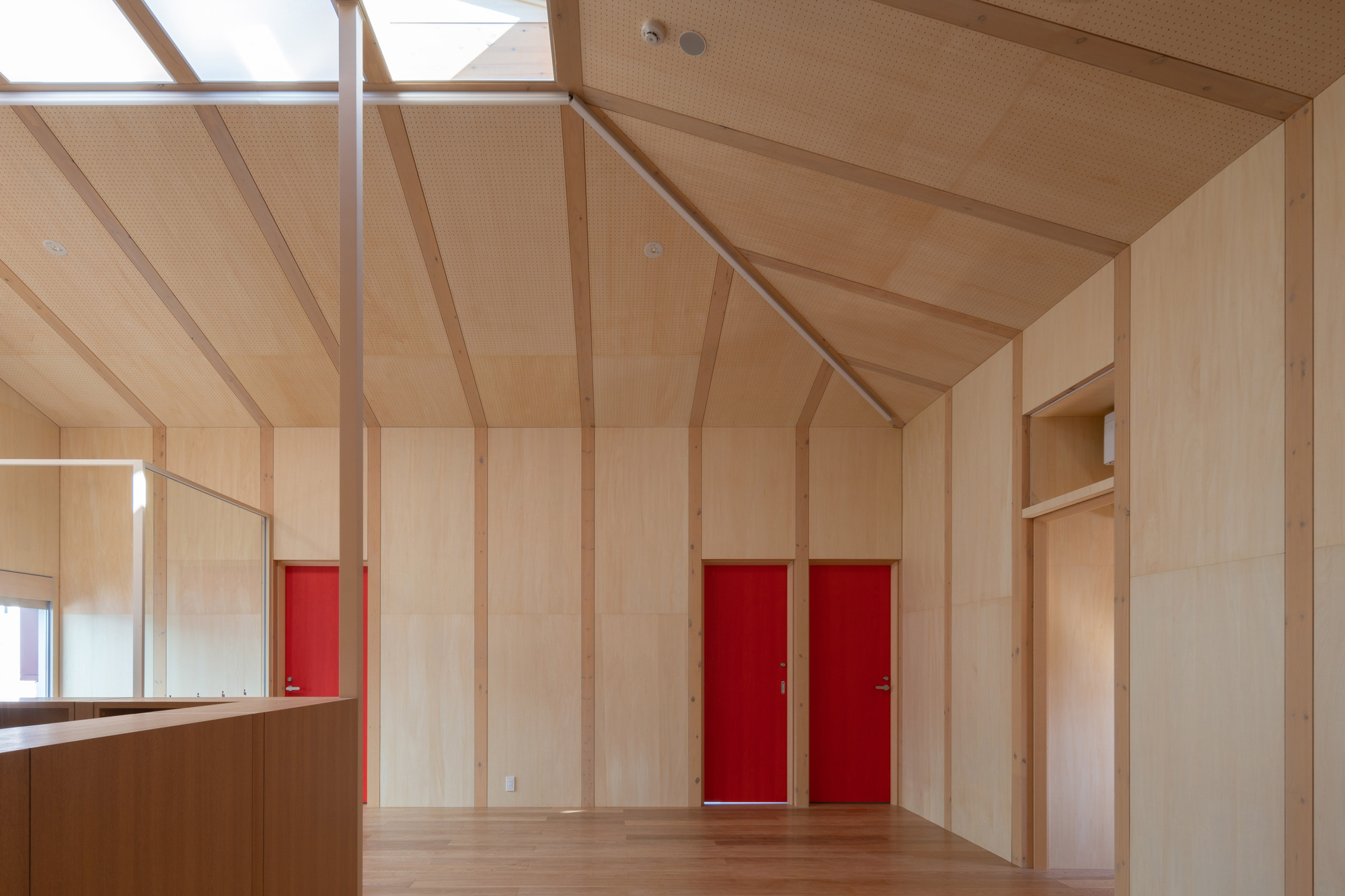 Plywood-lined room with vaulted ceiling, exposed timber ribs, and red sliding doors set into the wall