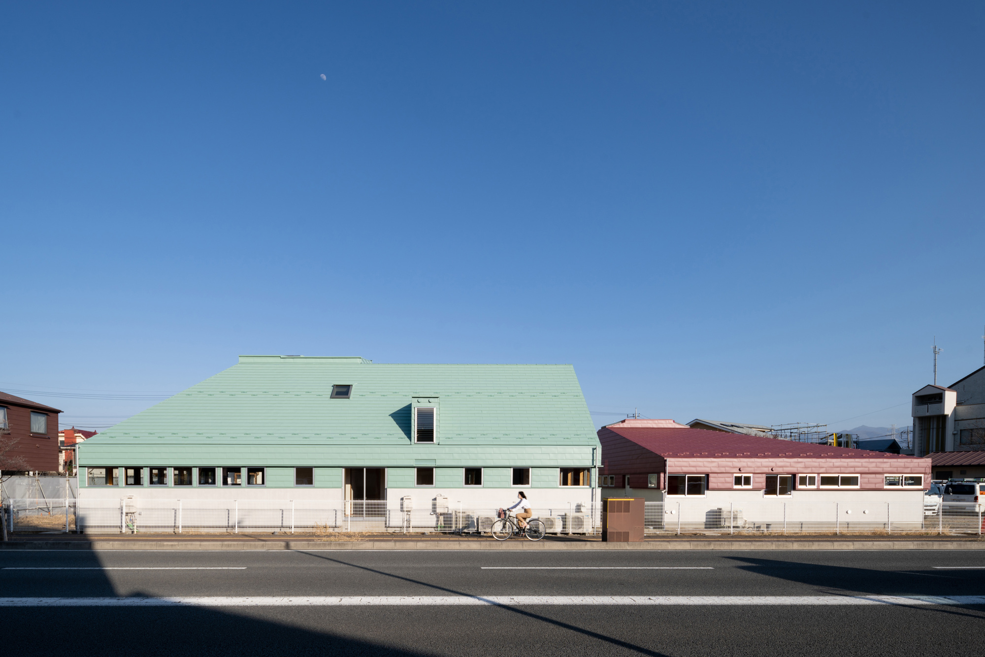 Street view of the building with a pale green pitched roof and continuous ribbon windows along the base