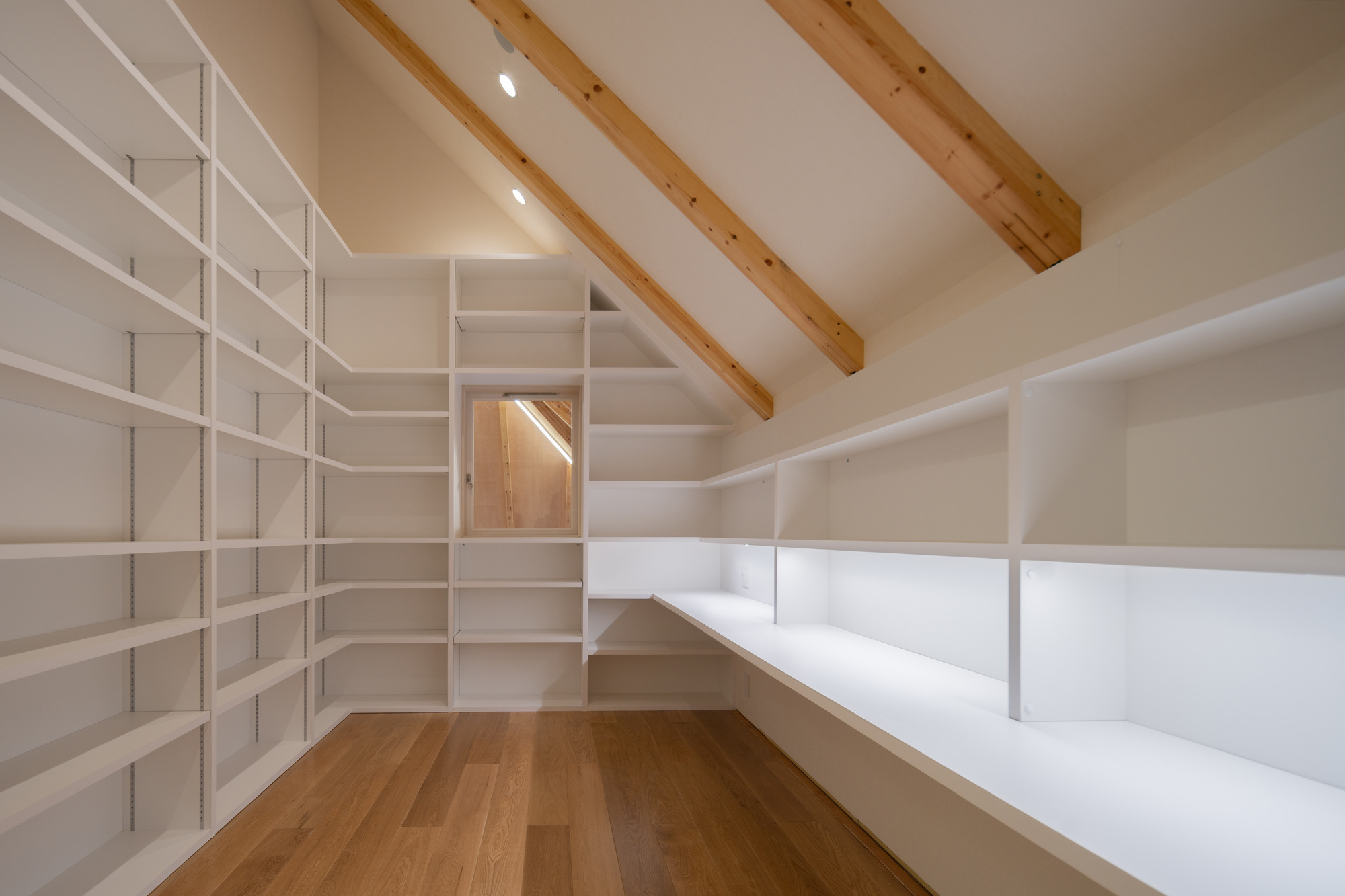 Corner of the library showing white modular shelving wrapping white walls beneath exposed timber beams