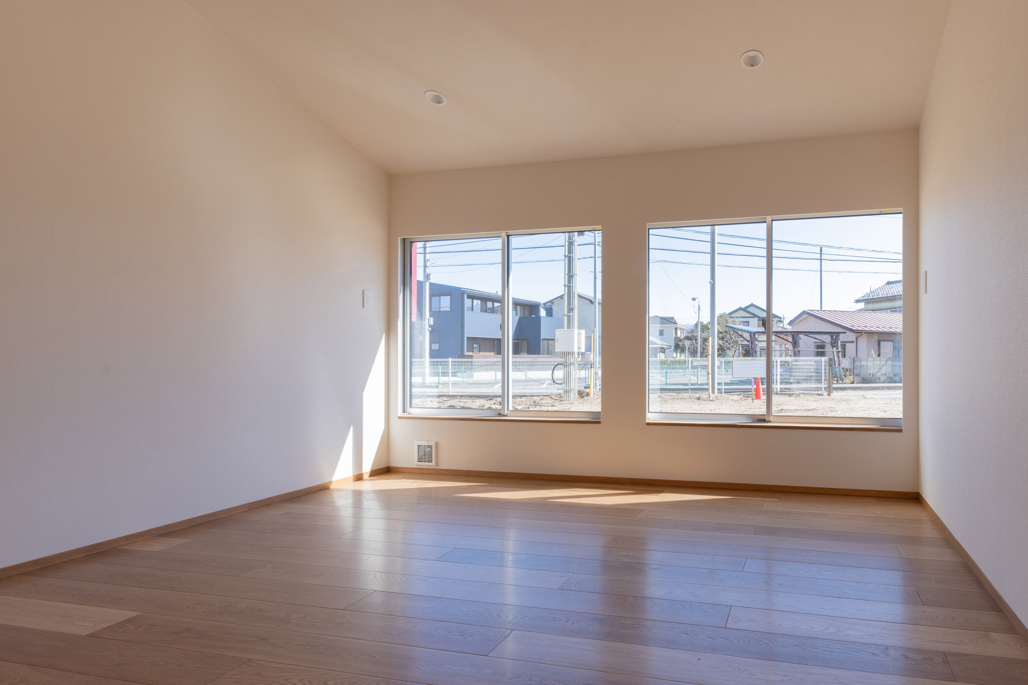 Empty room with pale wood flooring and paired windows casting angular sunlight across the floor