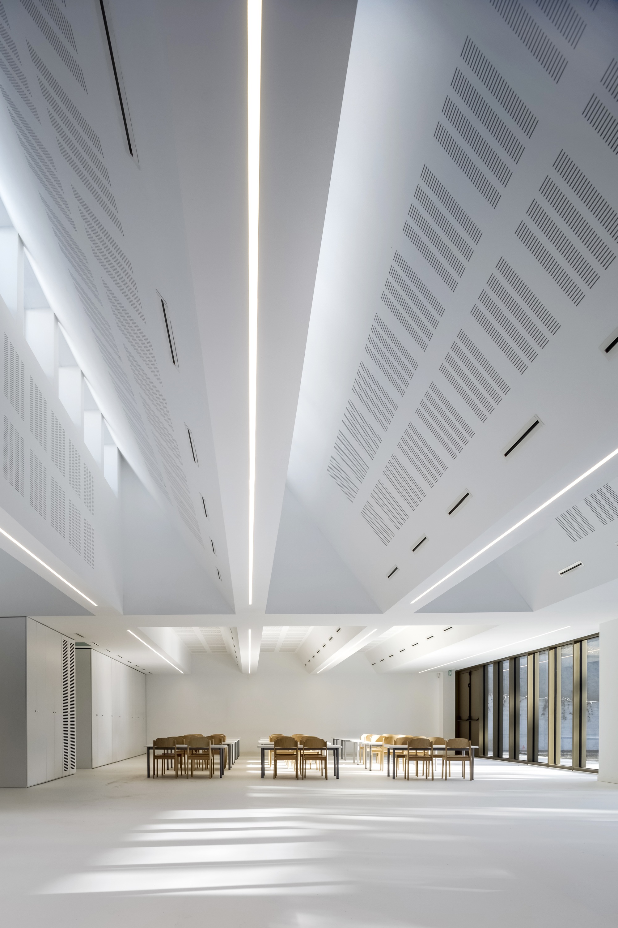 White ceiling with radial perforated panels and central skylight illuminating the white resin floor below