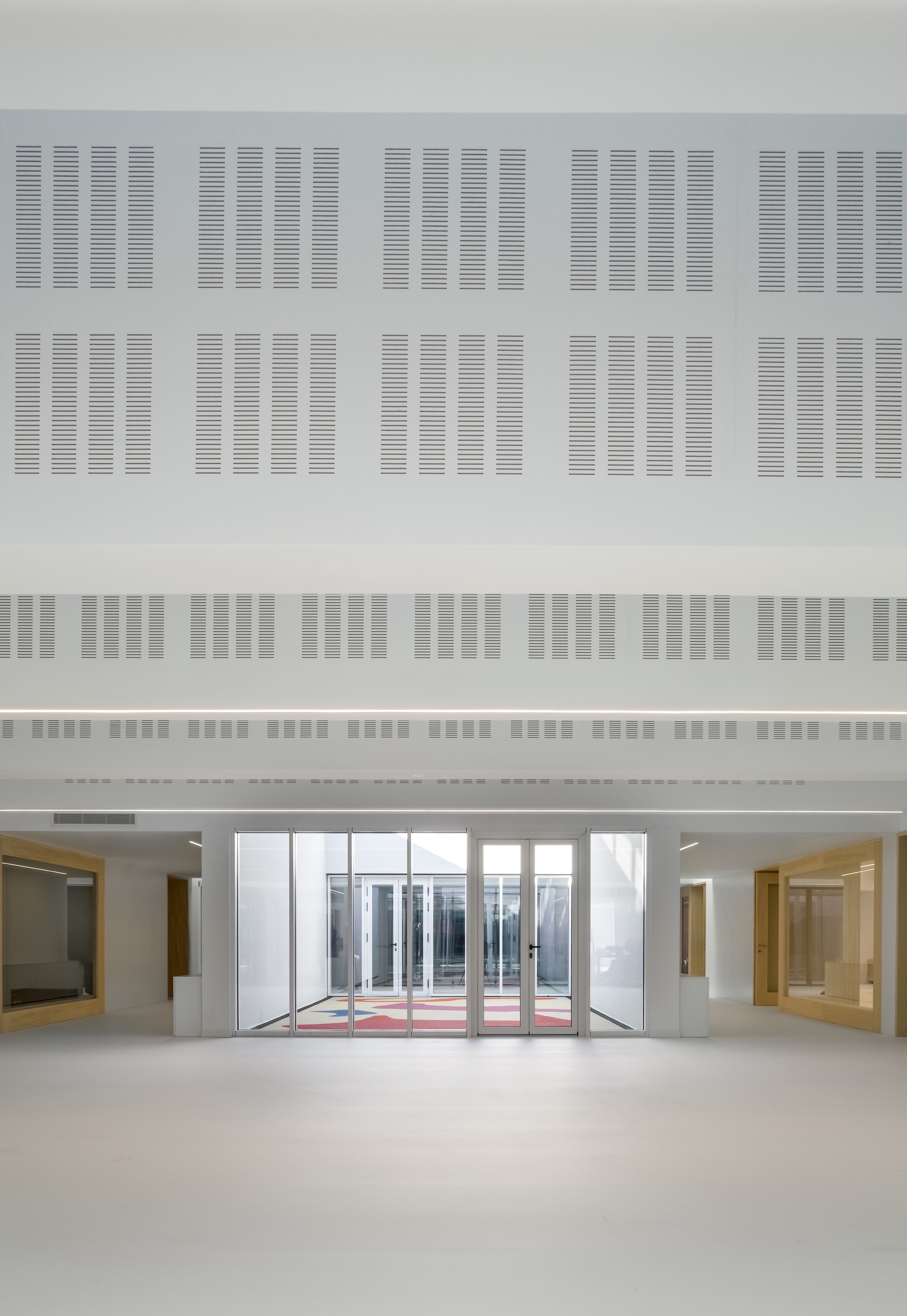 Interior lobby with glass entry doors facing a courtyard beneath a perforated acoustic ceiling