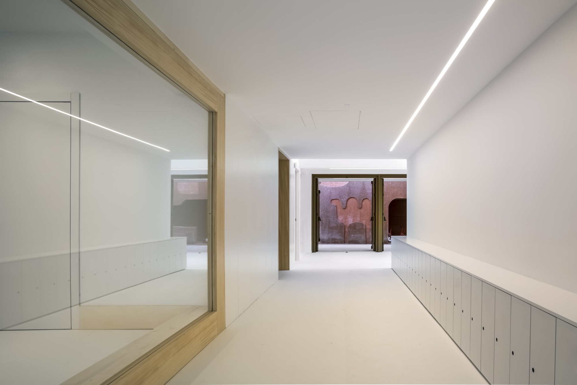 White corridor with timber door frames and rows of metal lockers leading toward windows