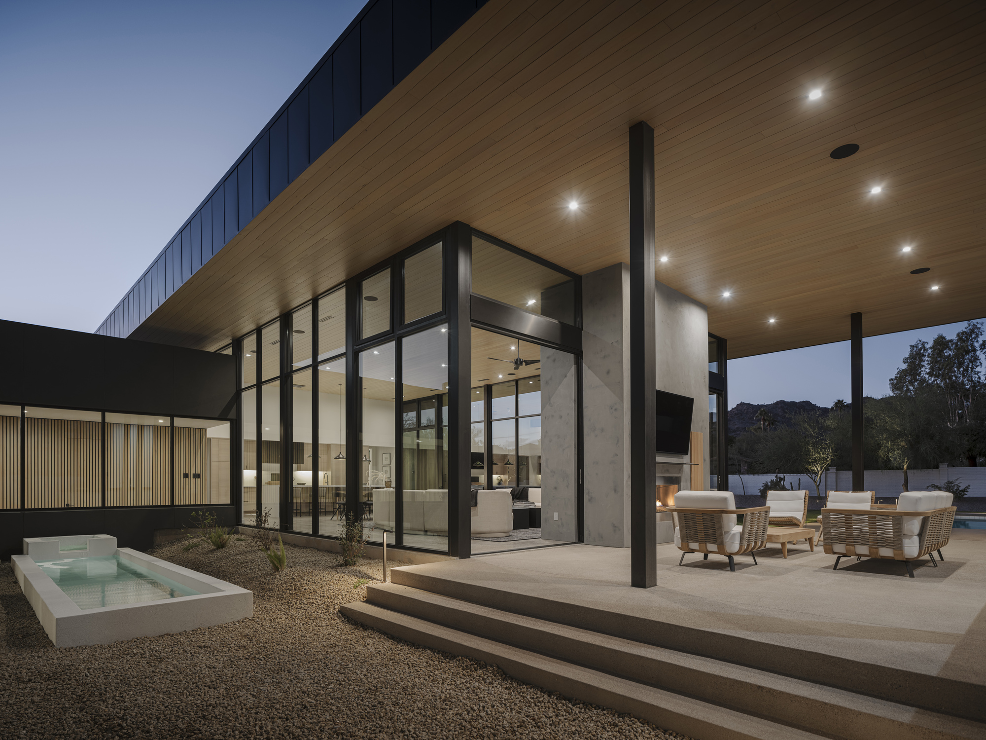 Covered terrace with timber soffit and black steel columns overlooking pool at dusk