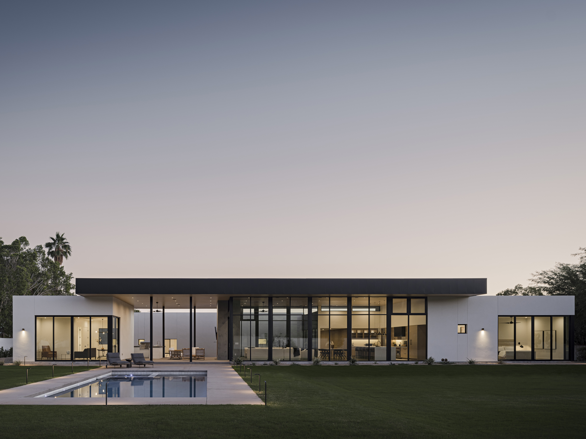 Garden elevation showing glass-walled living pavilion and swimming pool at dusk