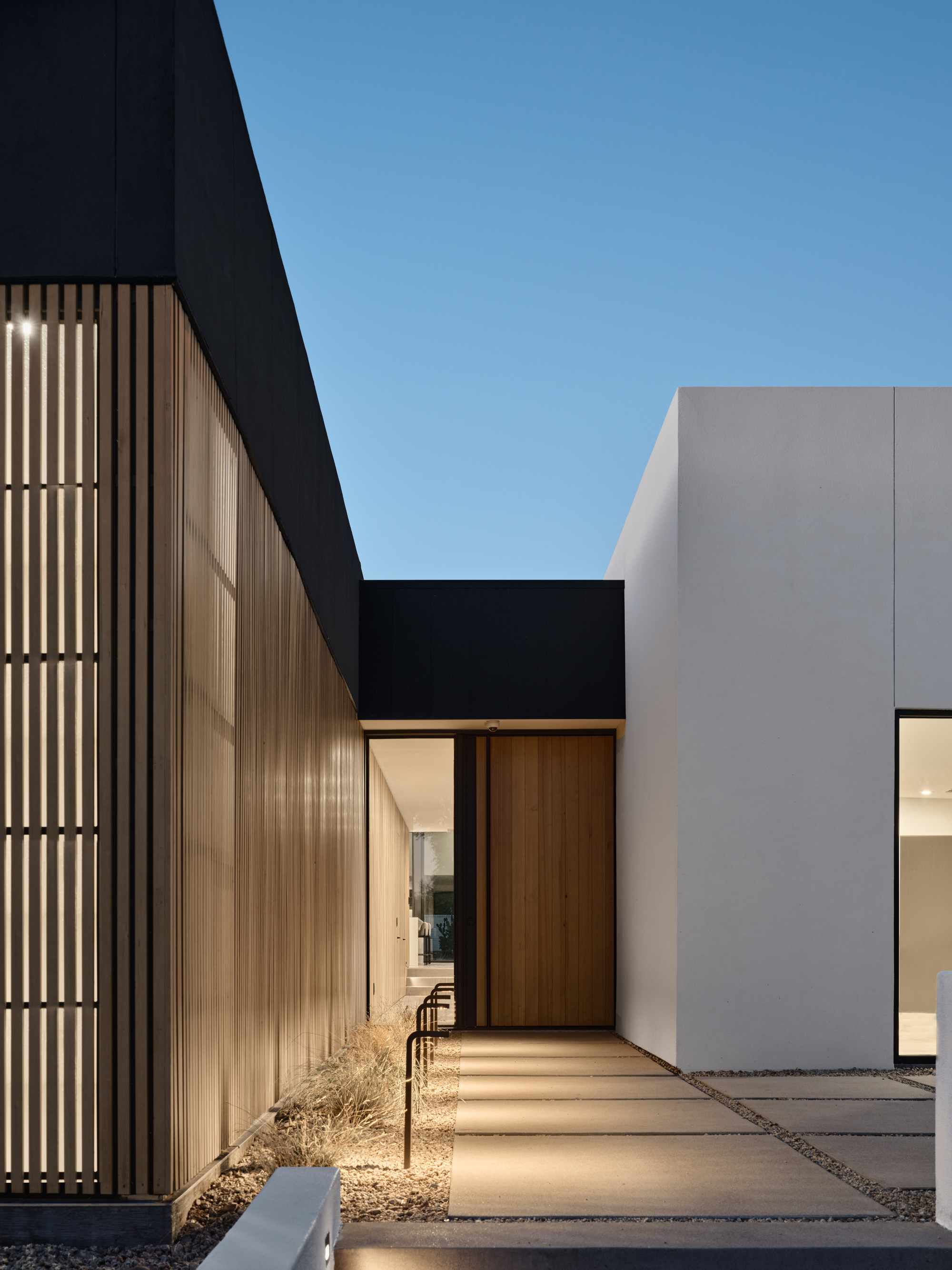 Entry courtyard with timber slat screen wall and paved walkway under clear sky