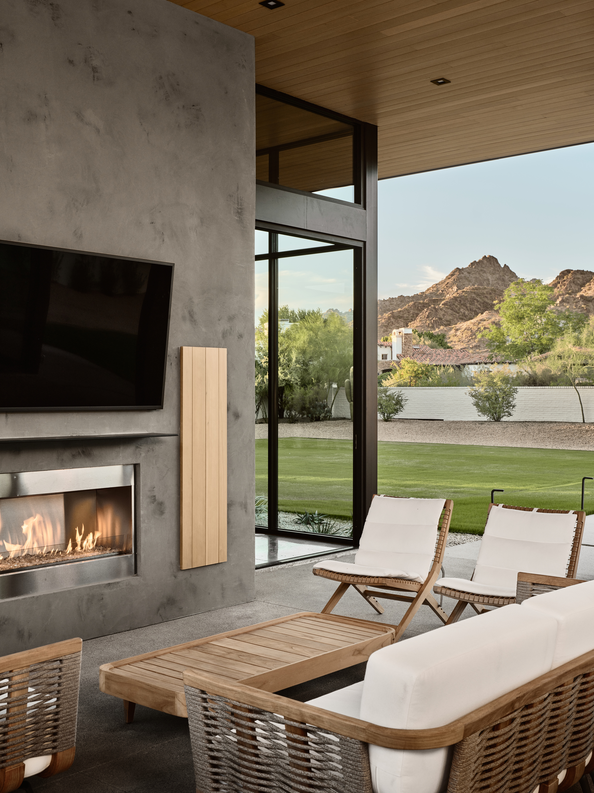 Living room with concrete fireplace wall and floor-to-ceiling glazing framing view of lawn and rocky hillside beyond