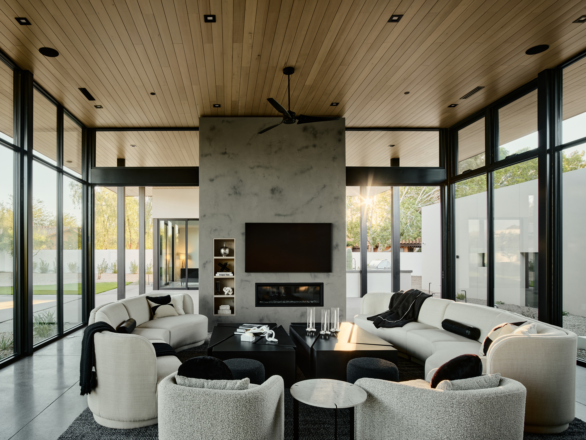 Open living space with central concrete fireplace volume flanked by full-height glazing and continuous wood ceiling plane