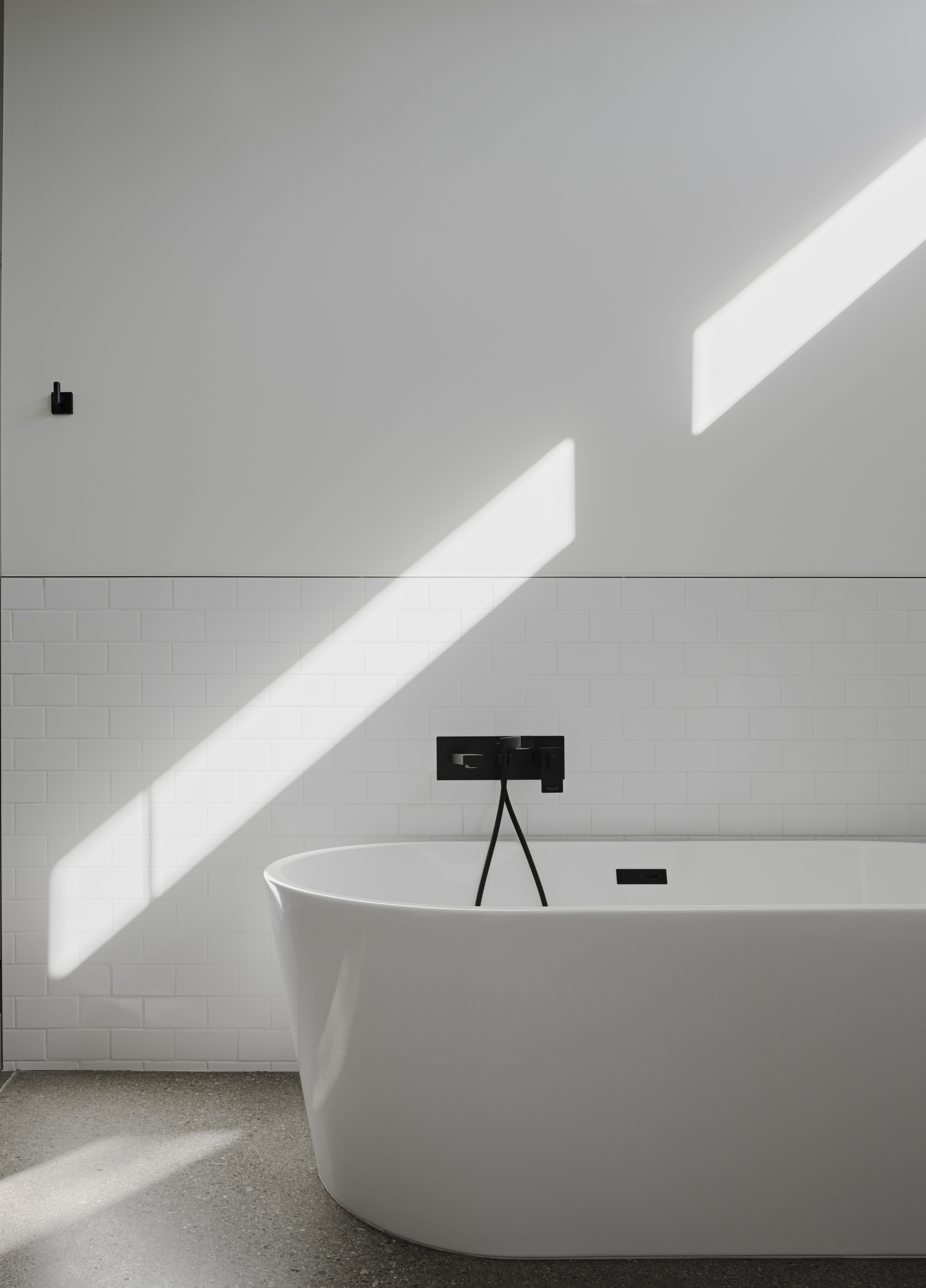 Freestanding white bathtub with black faucet under diagonal morning sunlight