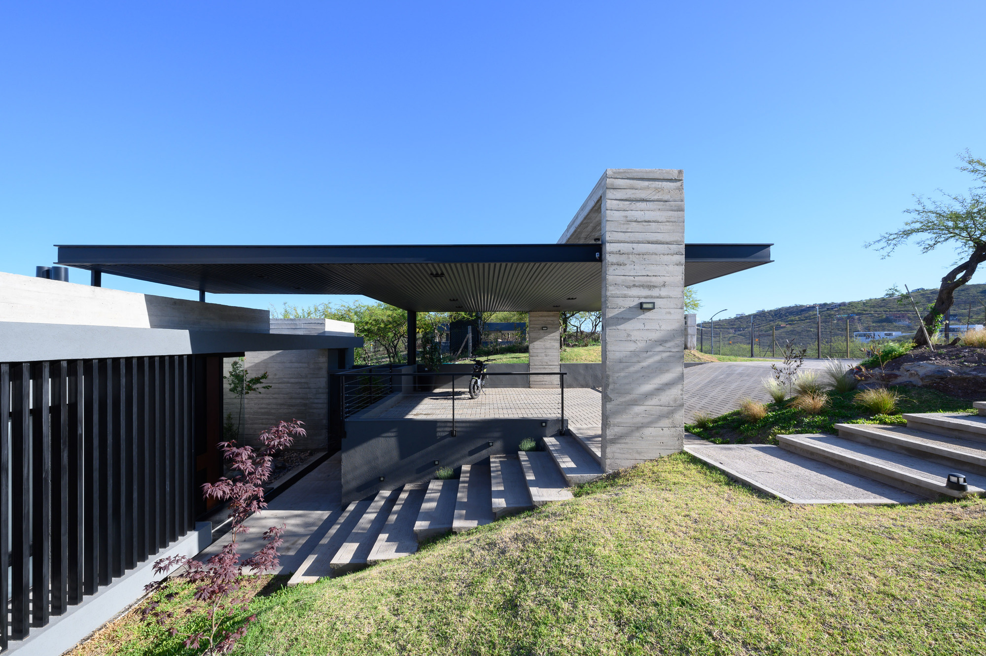 Cantilevered roof plane above board-formed concrete columns and a stepped entry pathway in full sun