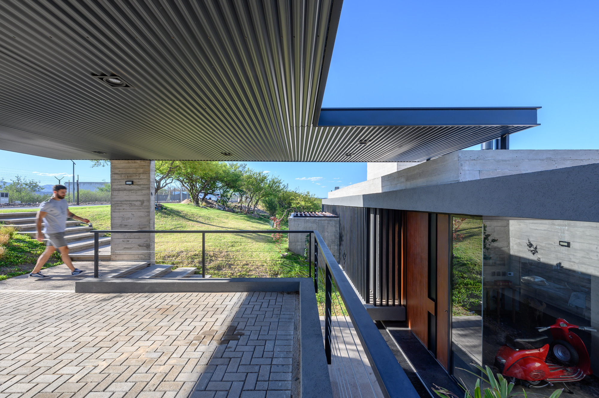 Covered terrace with corrugated metal soffit, stone chimney, and a figure walking beneath clear sky
