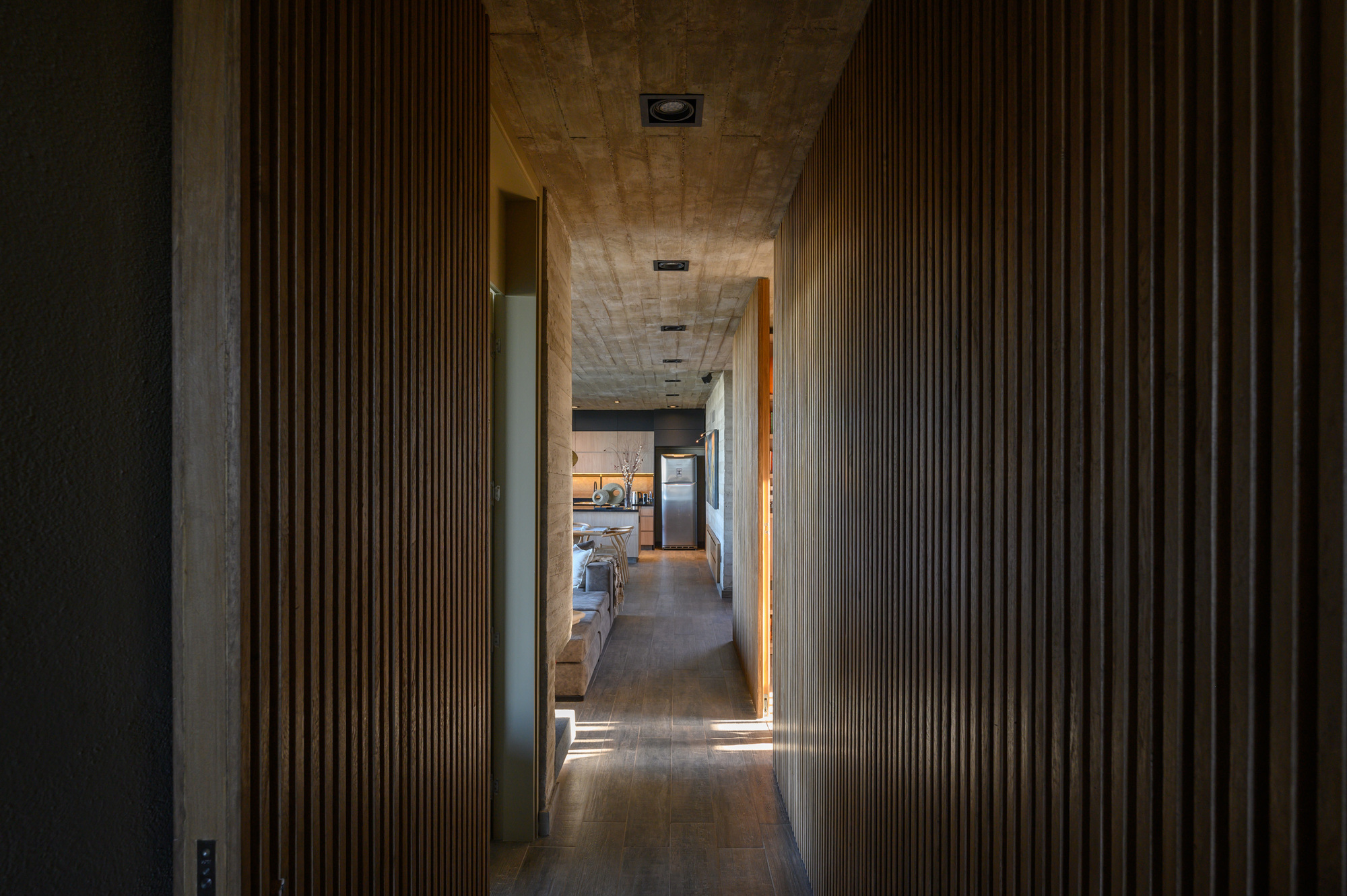 Interior corridor with vertical wood slat walls and timber ceiling leading toward a kitchen beyond