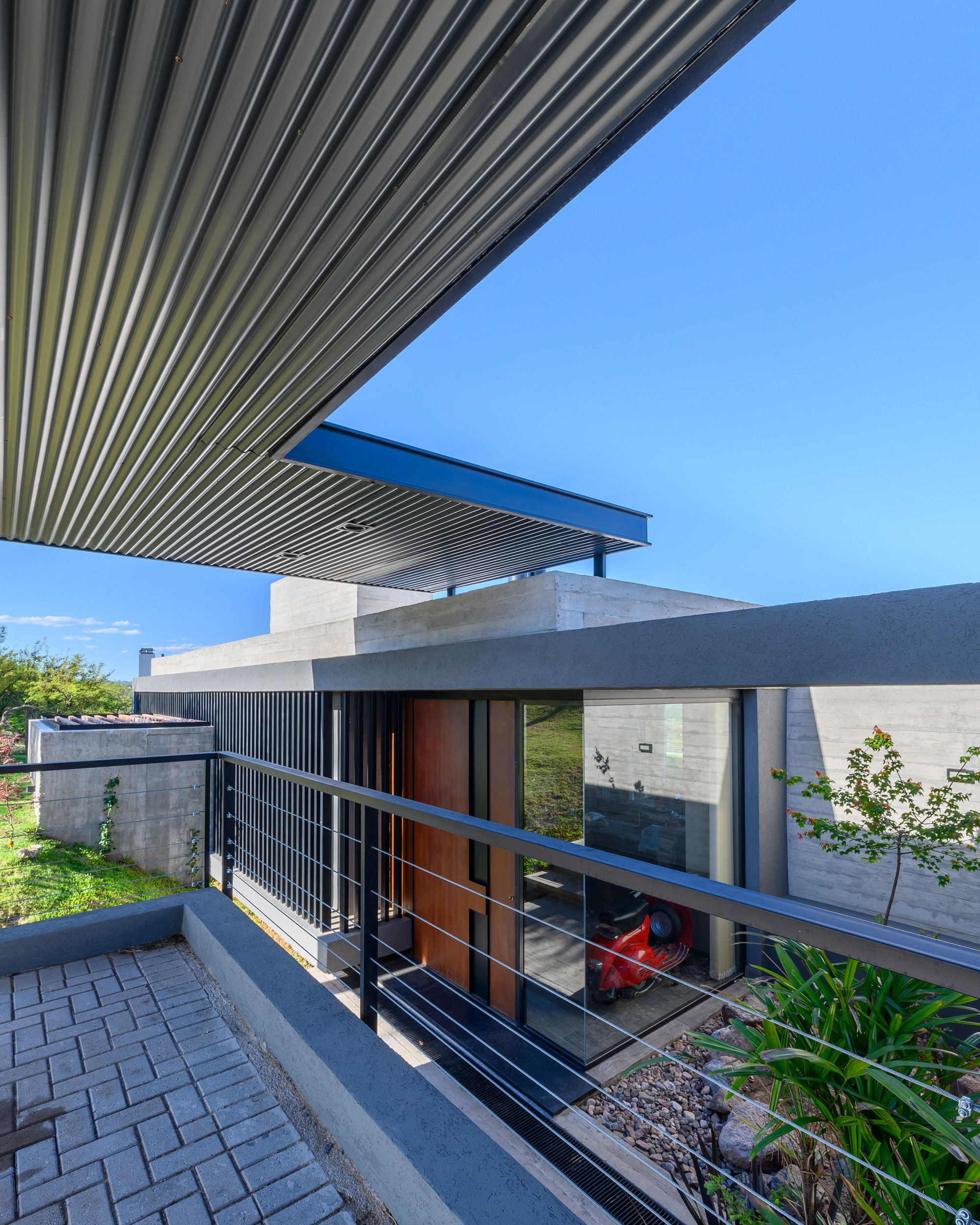 Exterior view showing cantilevered slatted canopy over glass-fronted entry with planted beds and paved driveway