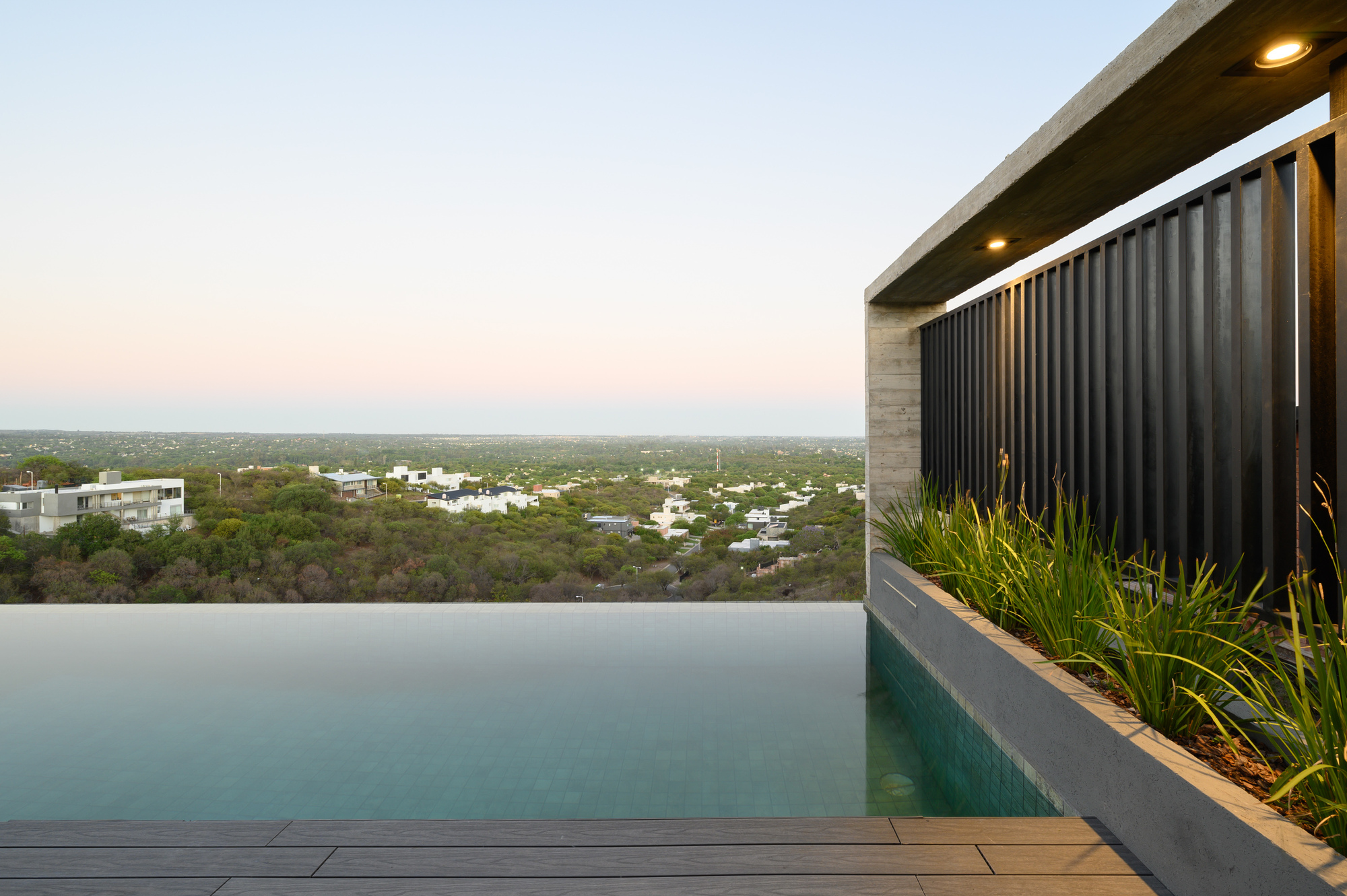 Infinity pool edge with vertical metal screen and timber deck at dusk with hills in the distance