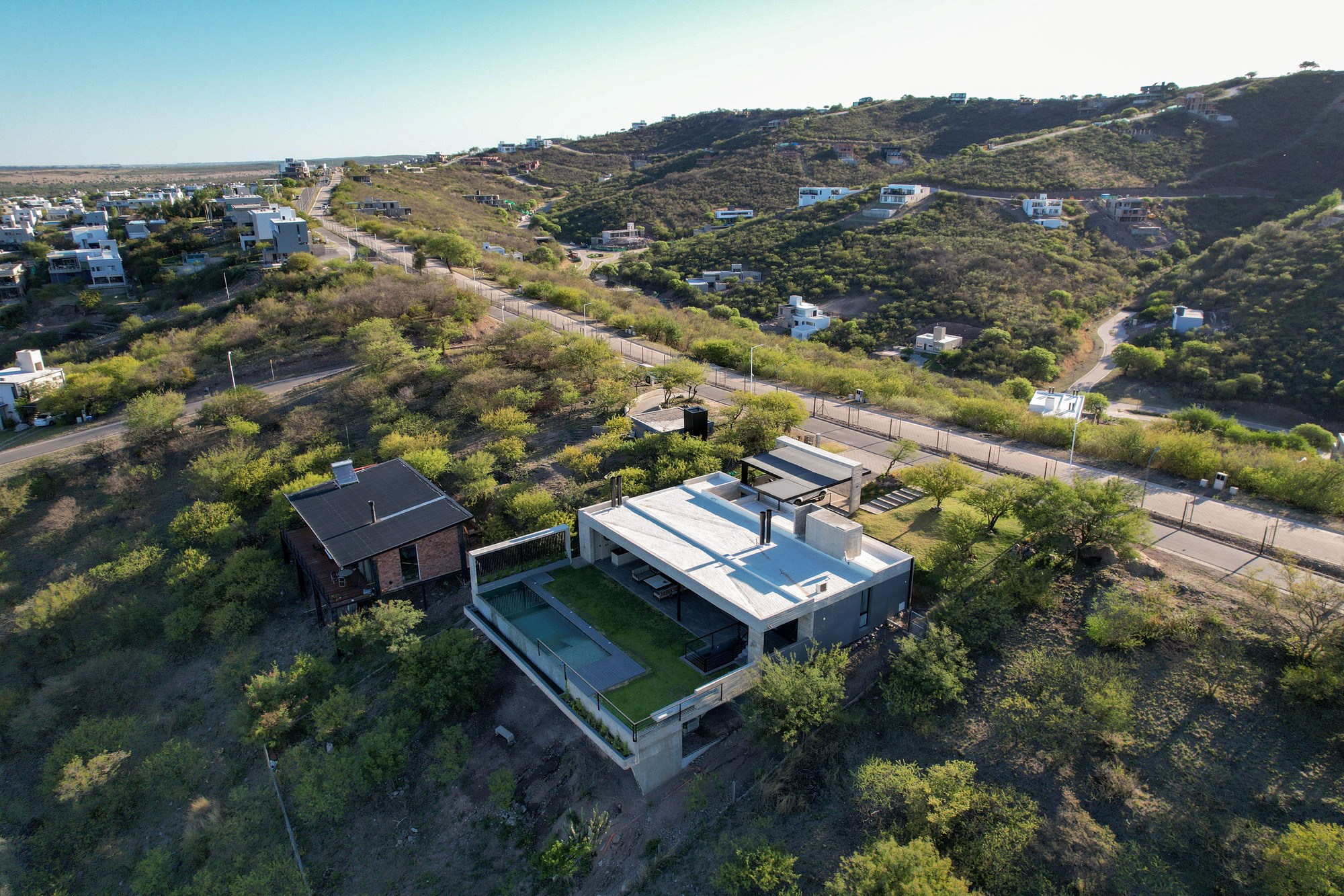 Aerial view of the concrete structure with rooftop pool set among sparse vegetation and hillside roads