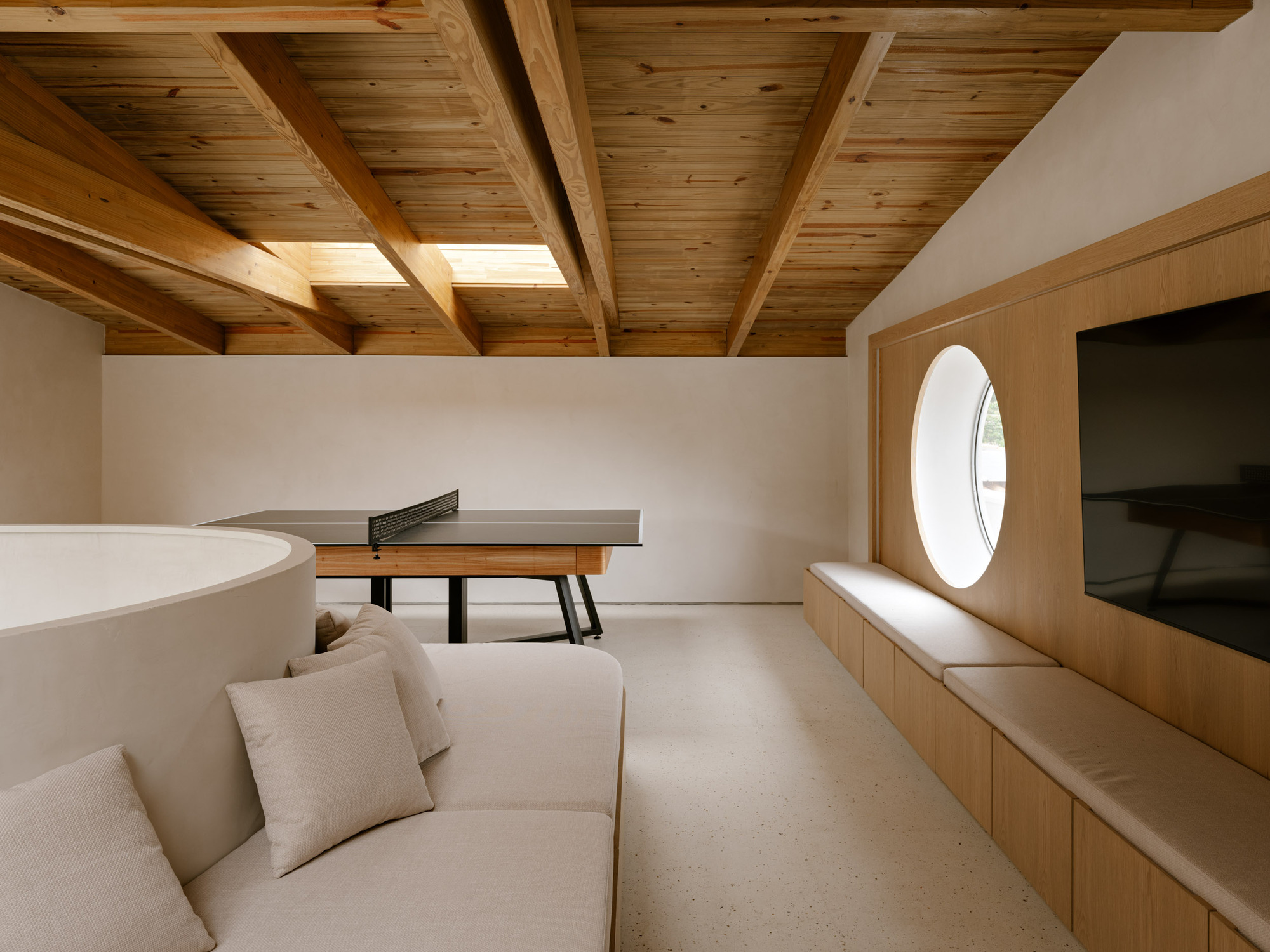 Upper level room with exposed timber ceiling beams, a circular window and built-in bench seating