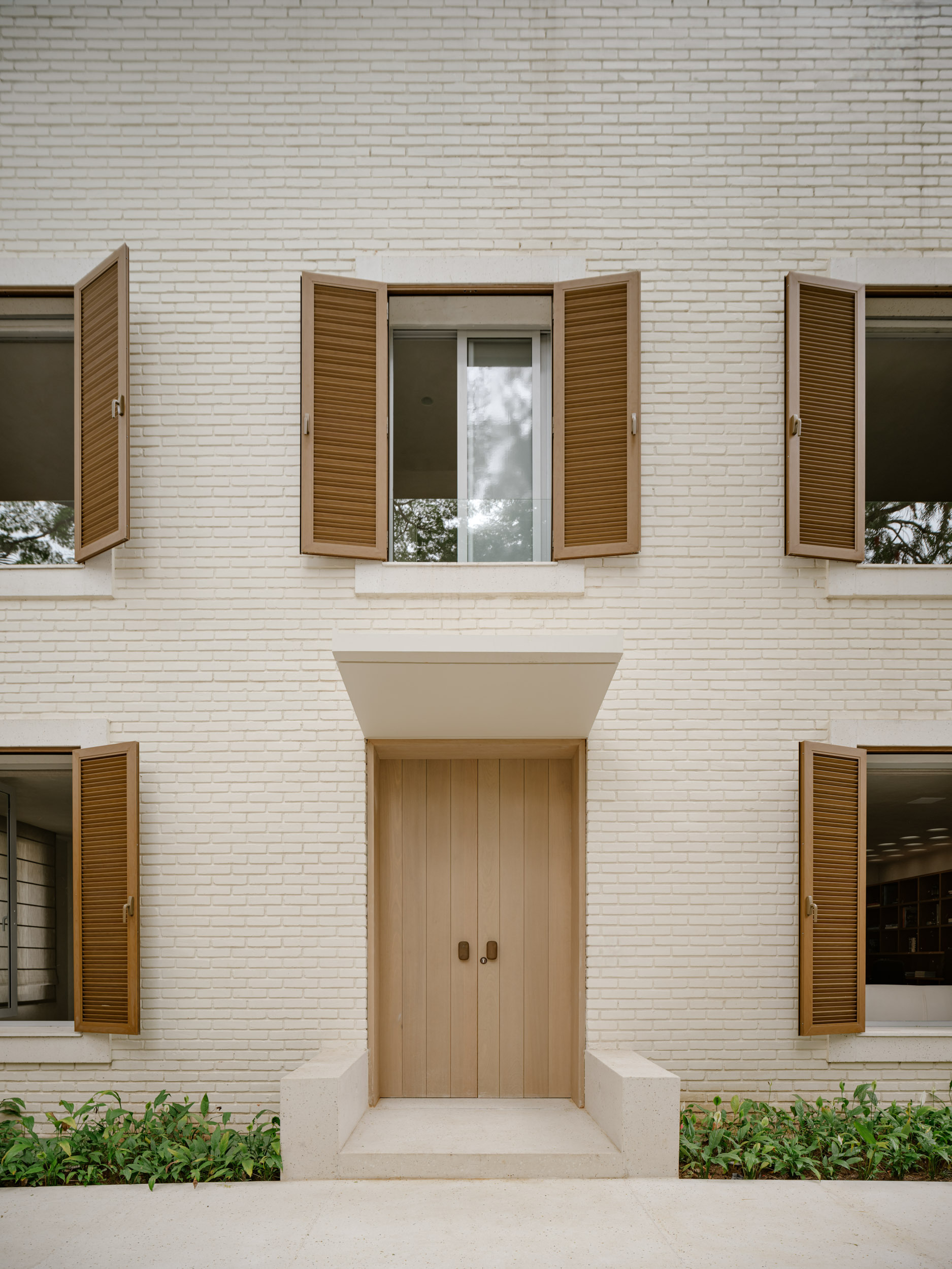 Symmetrical facade with white brick, recessed timber door and wooden louvered shutters flanking upper and lower windows