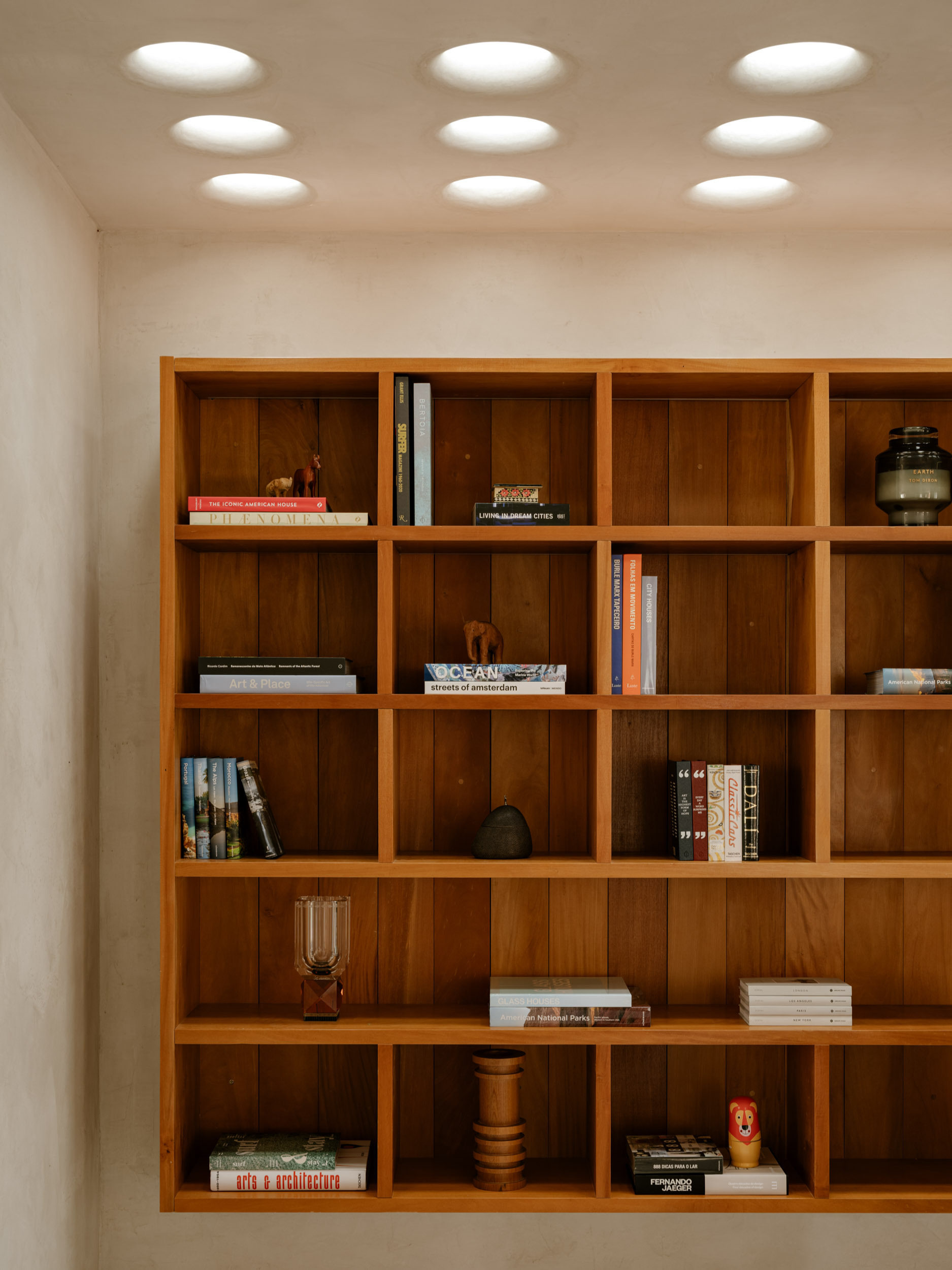 Built-in timber shelving grid with books and objects beneath a ceiling perforated with circular light wells