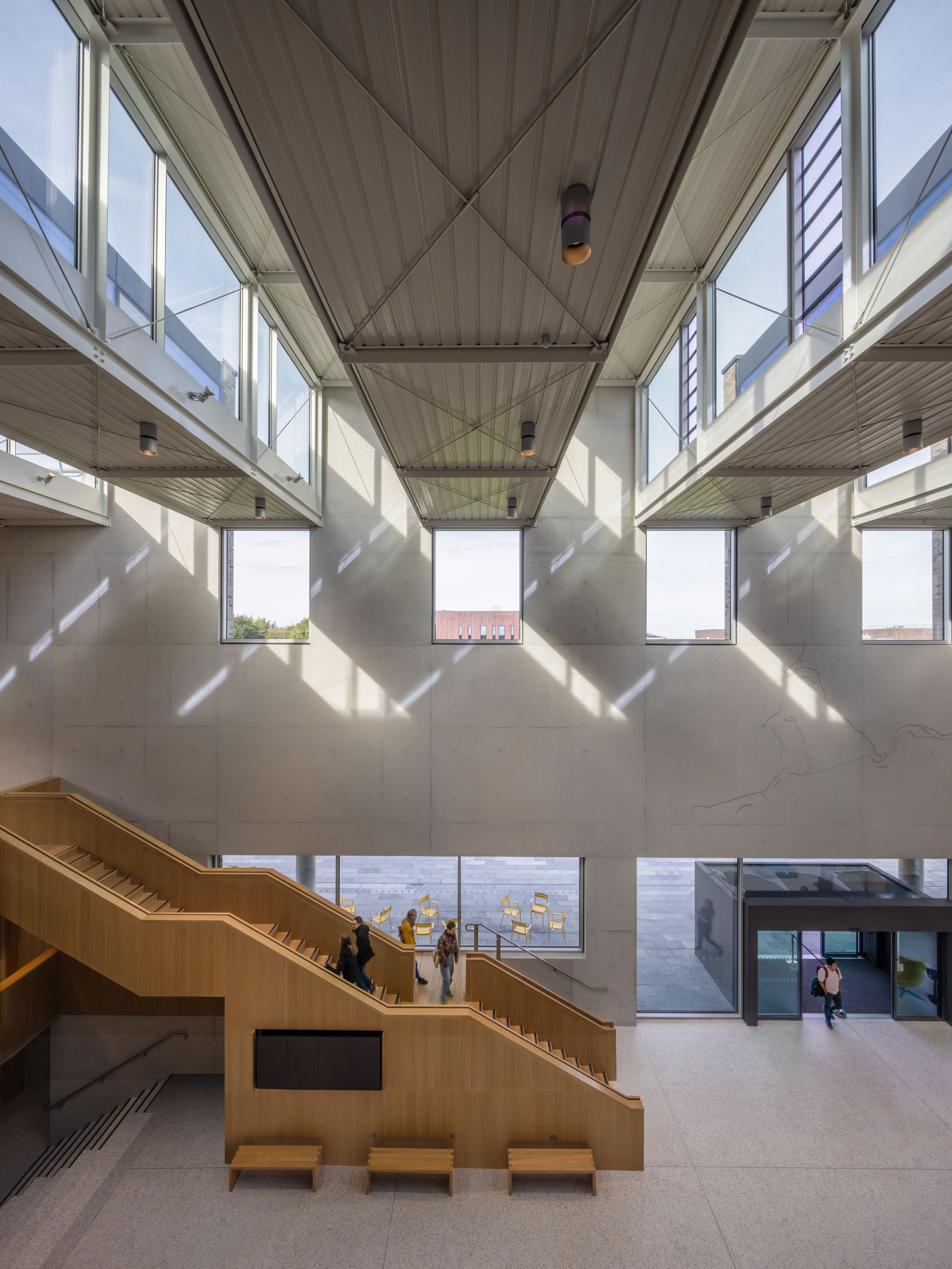 Four-story atrium looking down at timber staircase with diagonal light crossing suspended walkways and clerestory windows