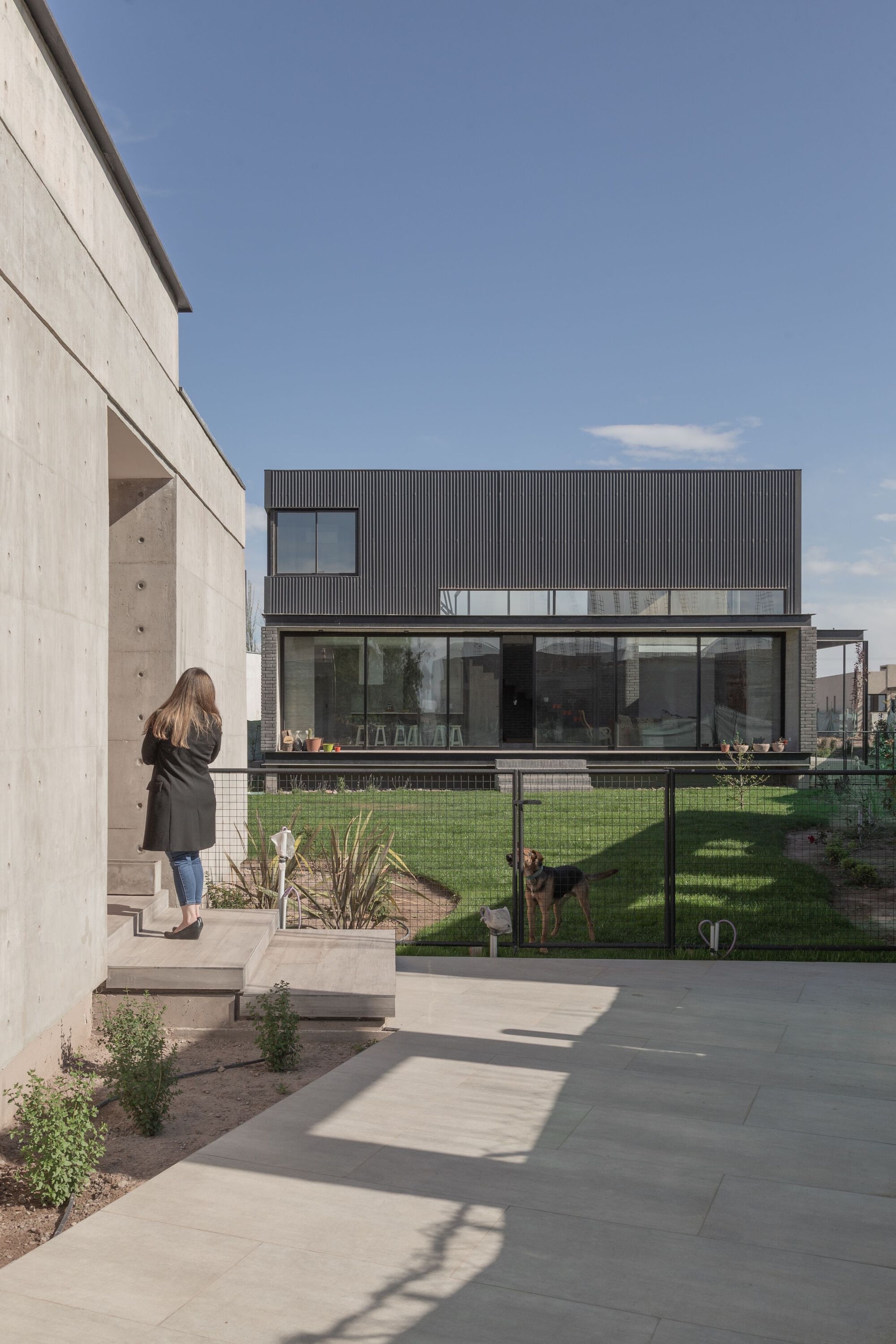 Concrete patio with large pavers leading to the glass-walled rear facade as a person walks down the steps