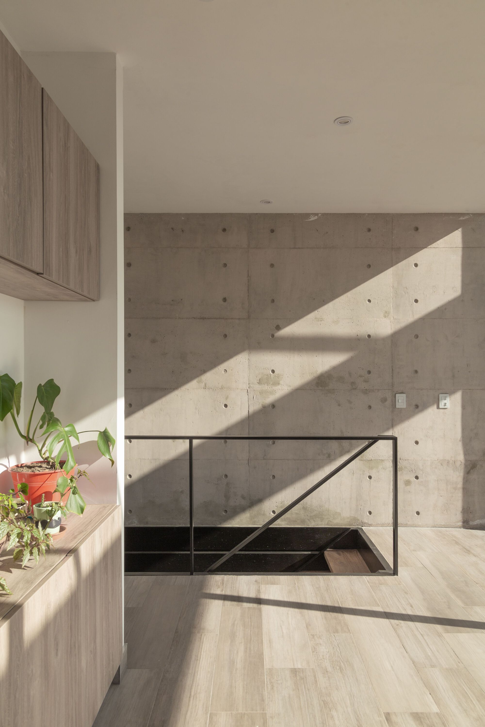 Board-formed concrete wall with diagonal shadows from sunlight streaming across the light wood floor