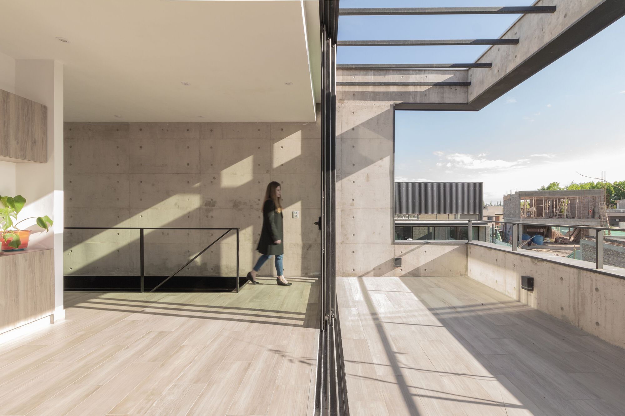 Upper-level terrace with concrete walls and glass railing where a person walks under the skylight opening