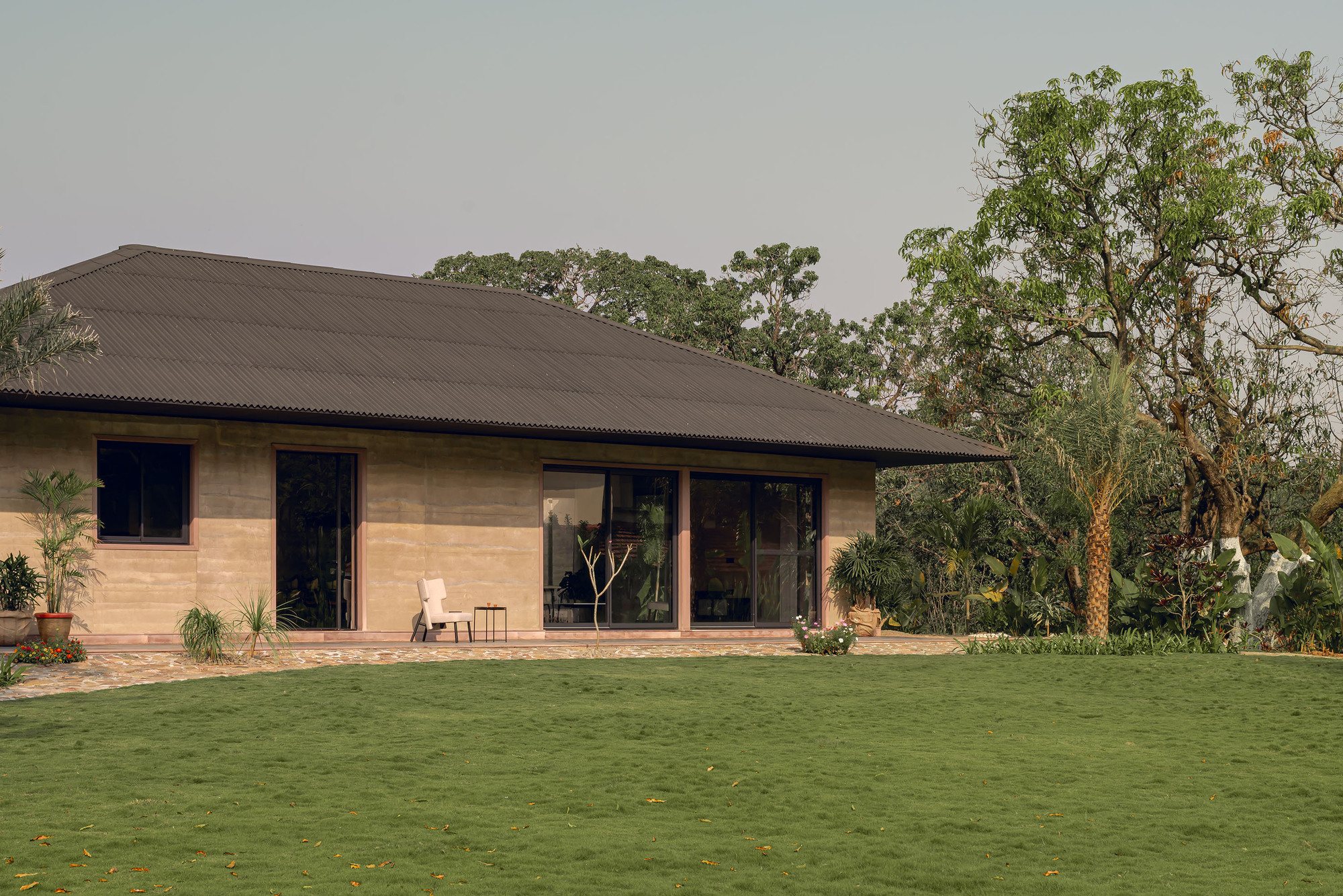 Corner view of the glazed terrace and rammed earth walls with paved patio and surrounding vegetation