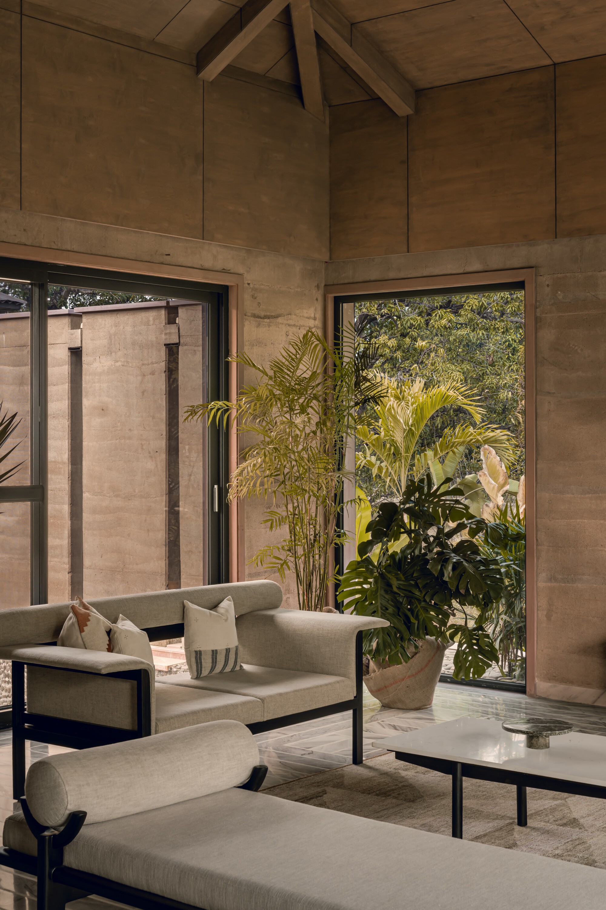 Double-height living room with exposed timber ceiling trusses and floor-to-ceiling glazing framing garden views