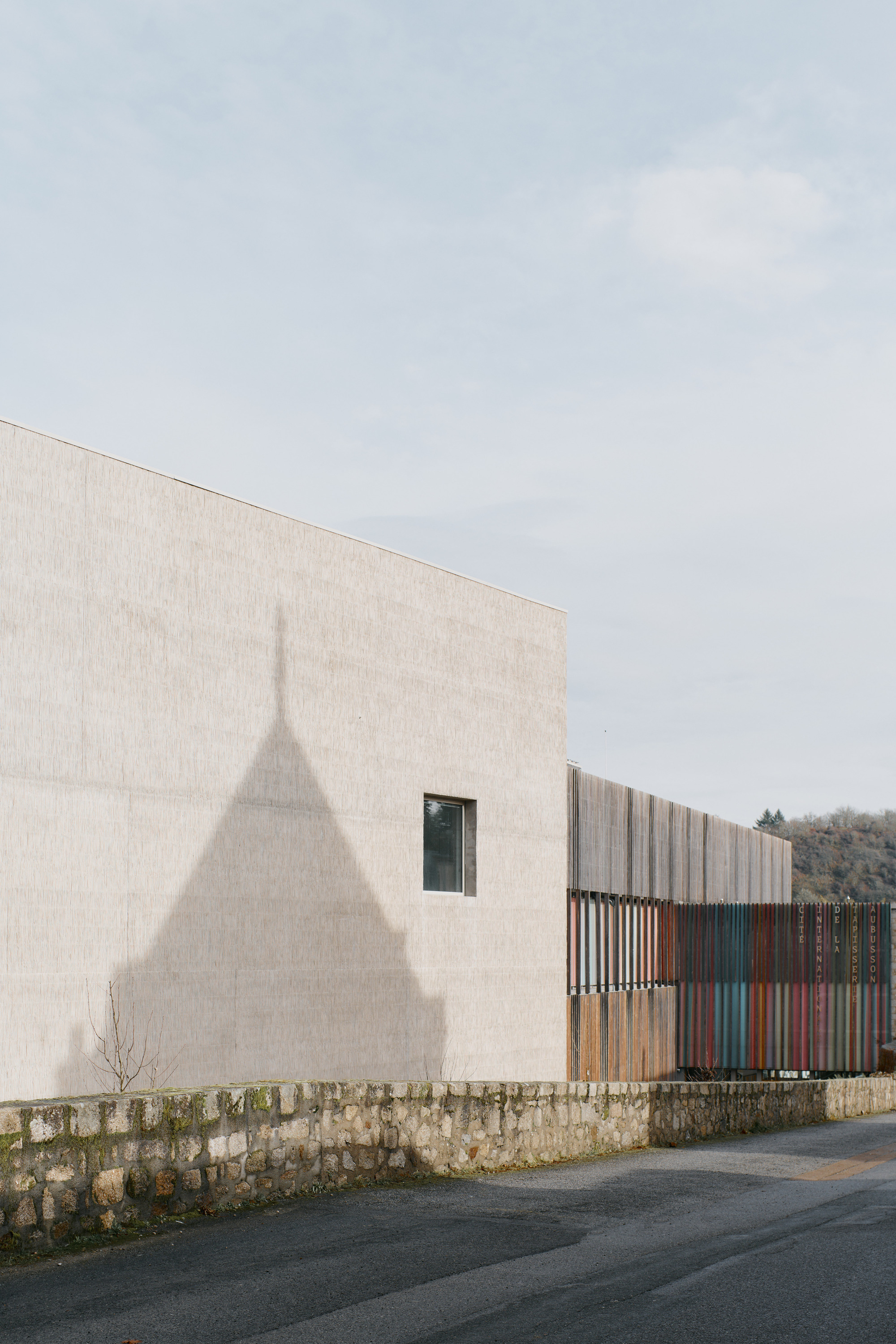 Shadow of a tower cast on pale concrete wall above a low stone wall