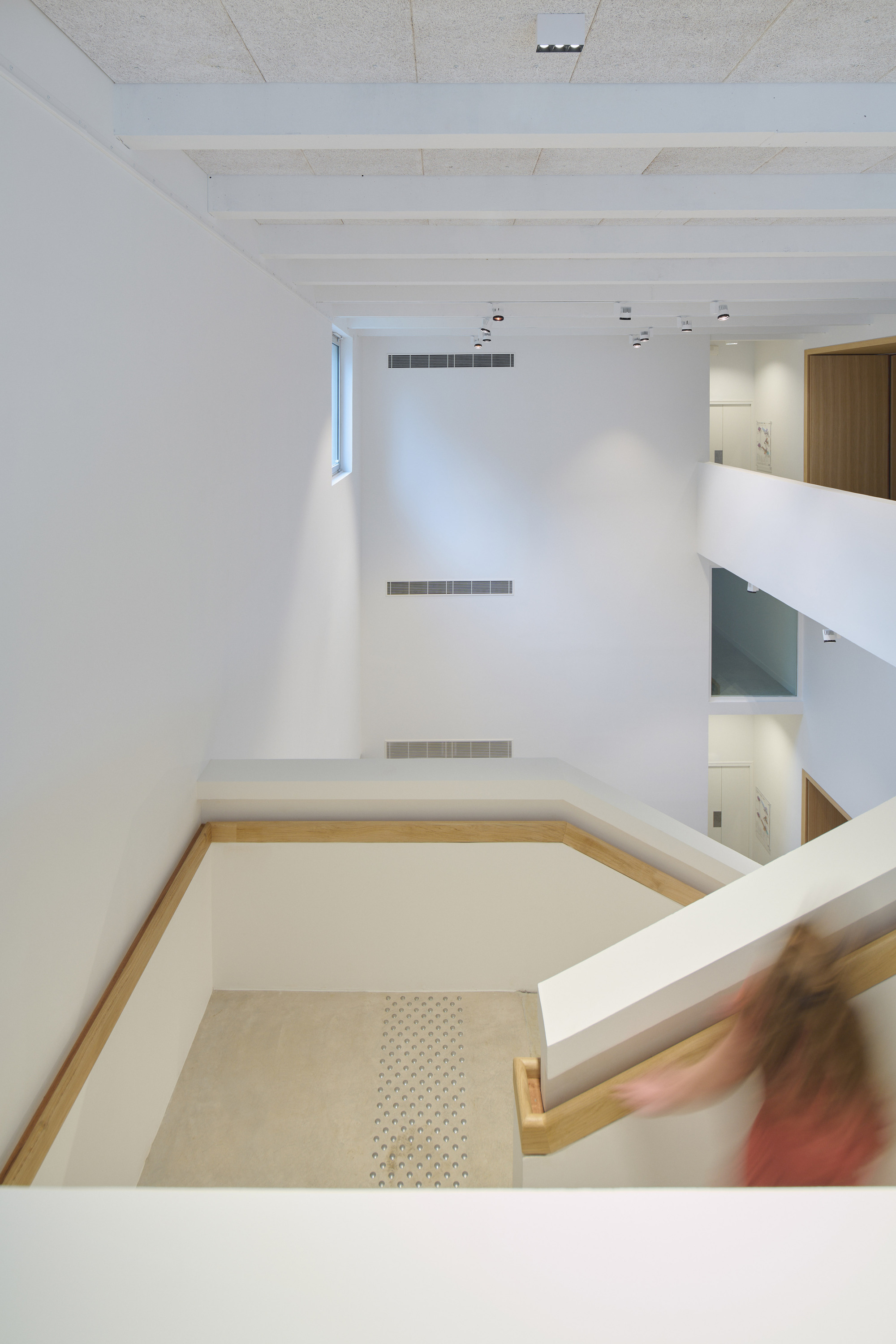 Looking down into a double-height stairwell with white walls and a figure descending the handrail