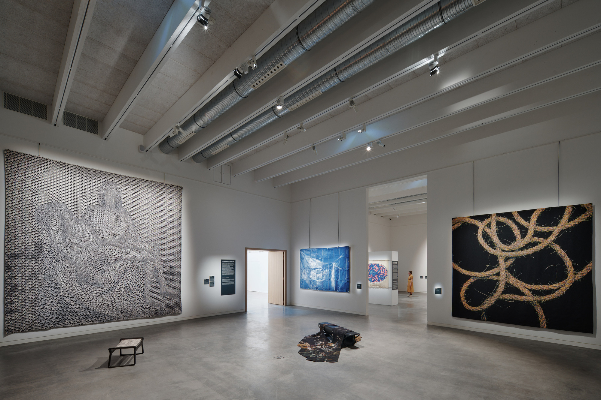 Open gallery space with exposed mechanical systems along concrete ceiling and large-scale artworks on white walls