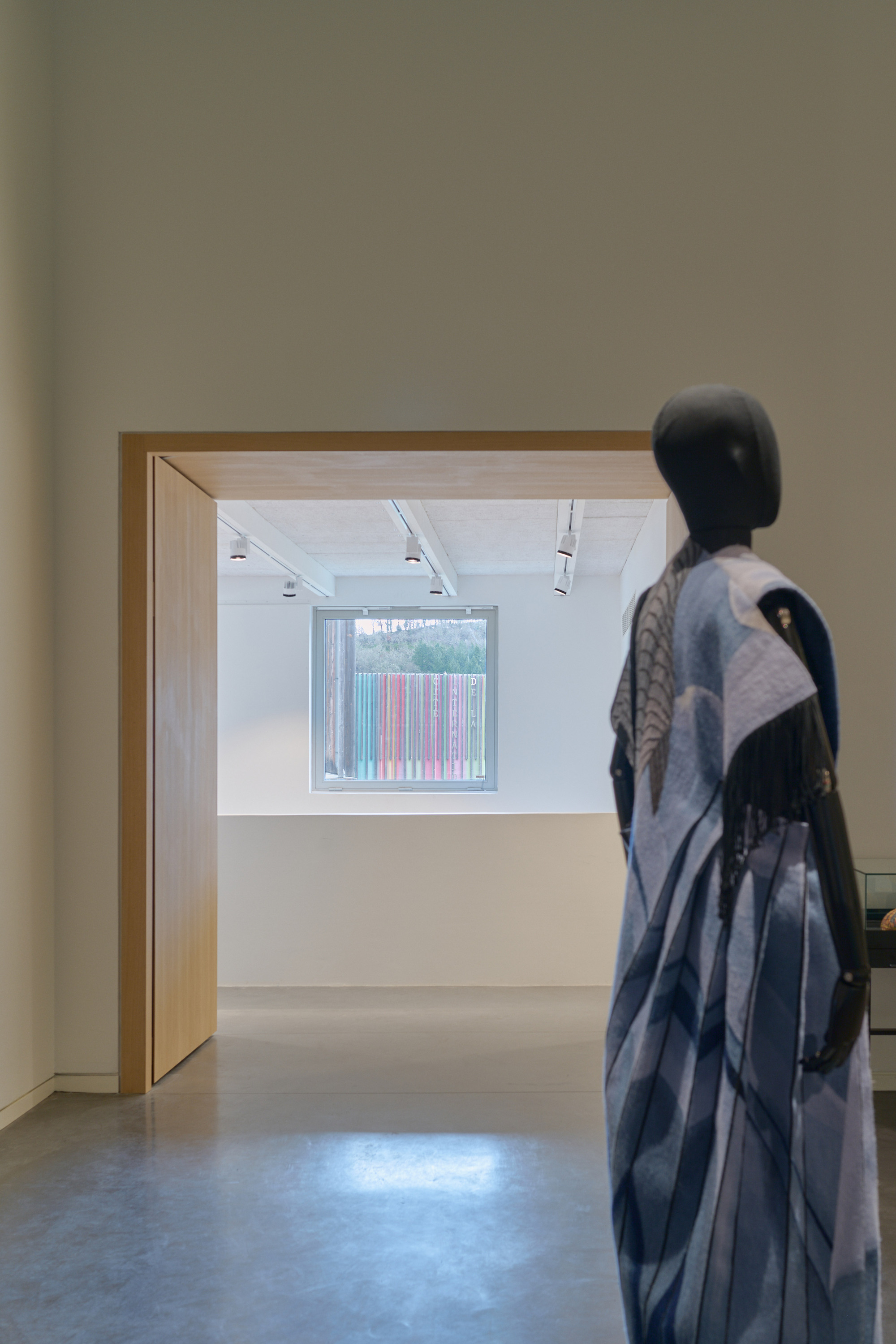 Gallery view through timber doorway with sculpture in foreground and window framing trees beyond