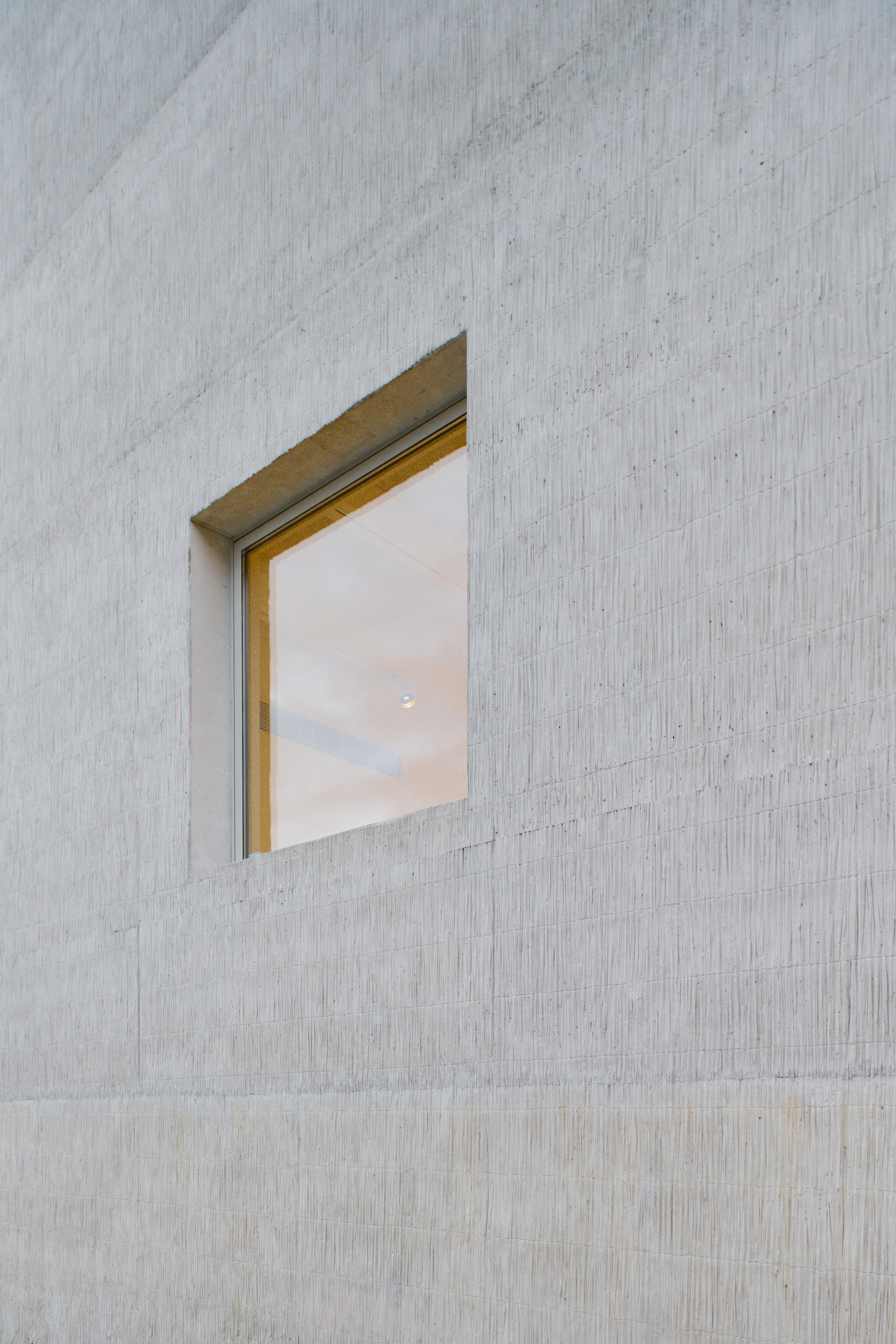 Recessed window with brass frame set into a pale concrete facade with vertical formwork texture