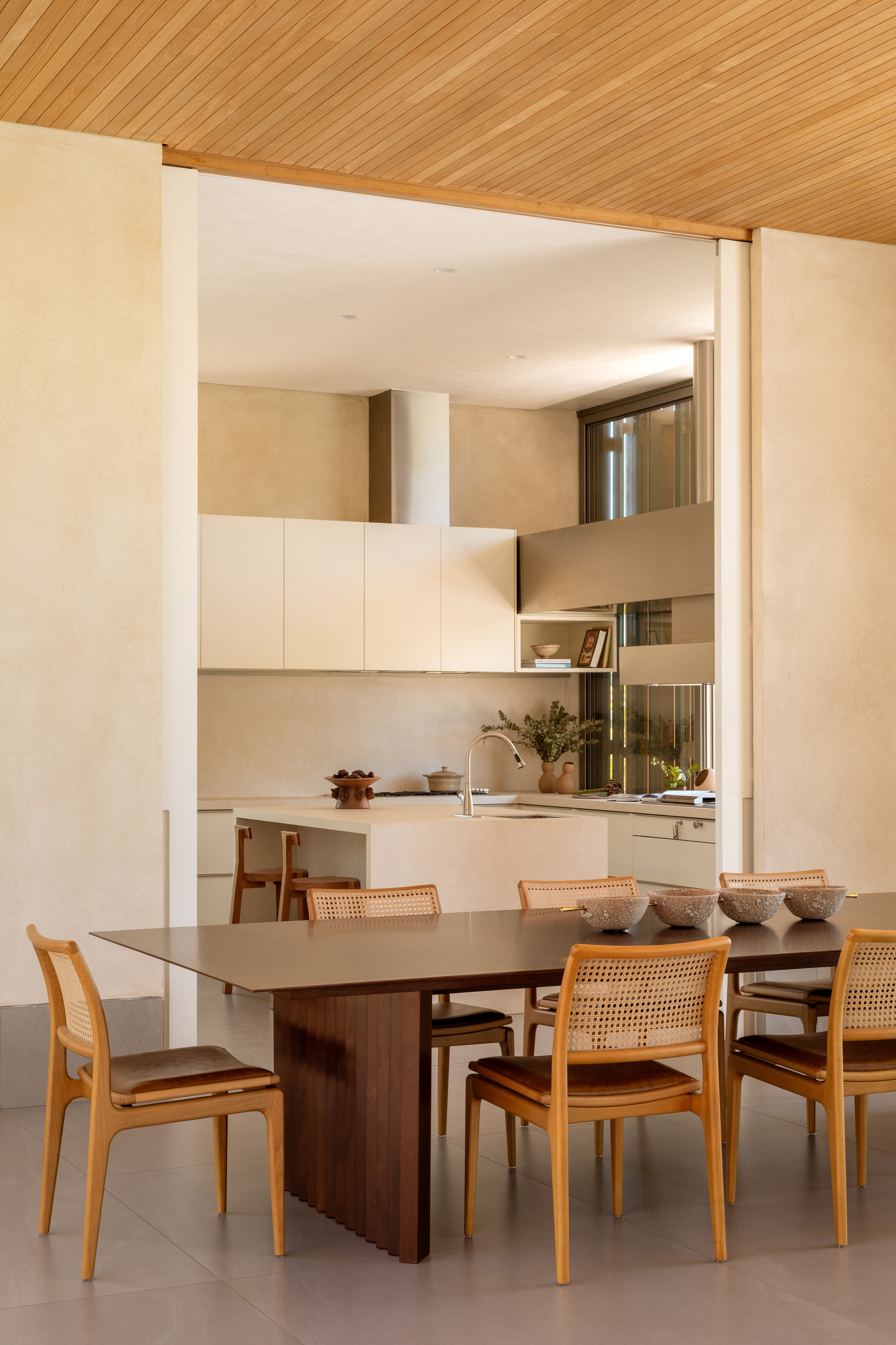Dining area with cane chairs beneath timber ceiling beams looking through to the kitchen beyond