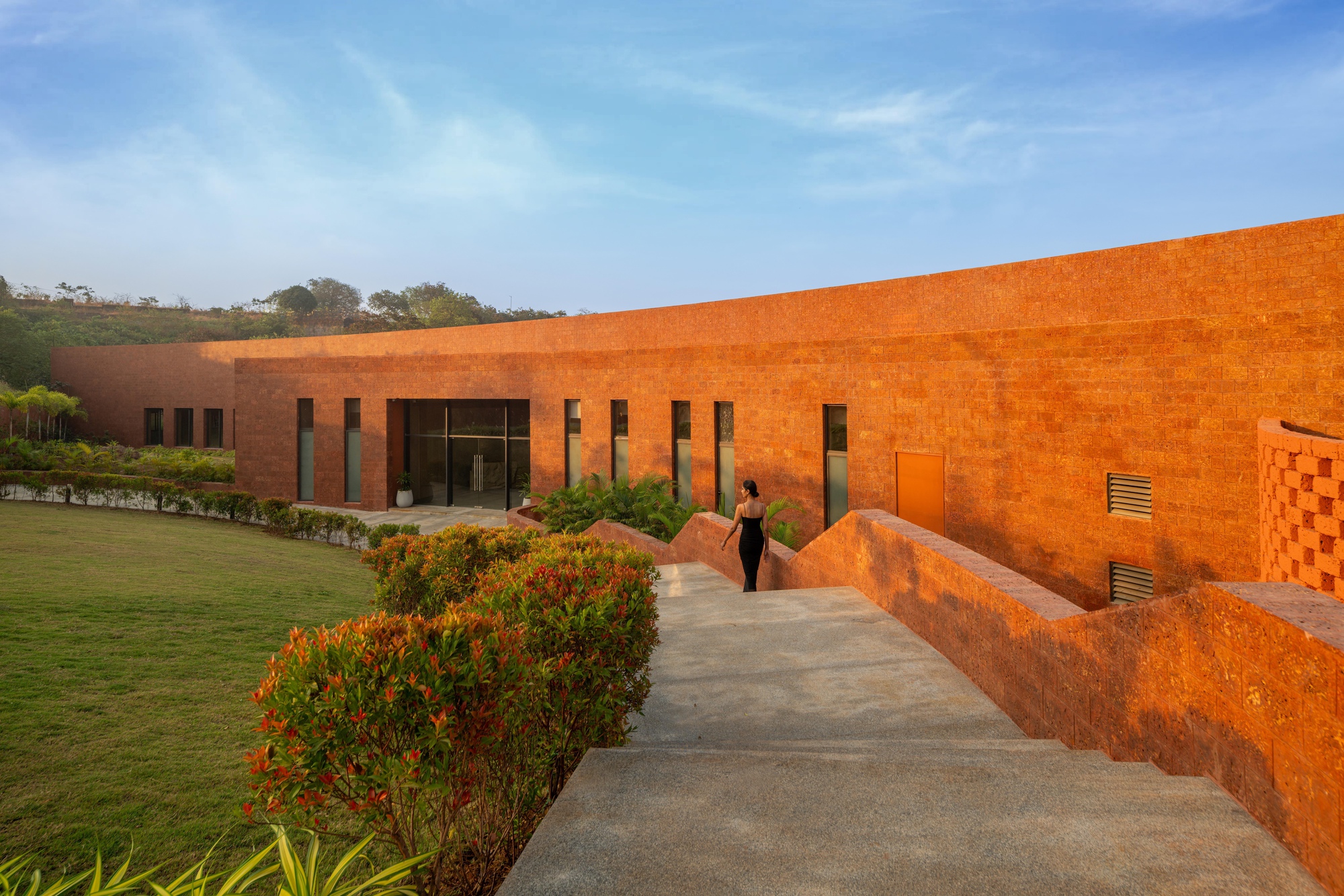 Pathway between the rammed earth wall and planted bed leading to the glass entrance at dusk