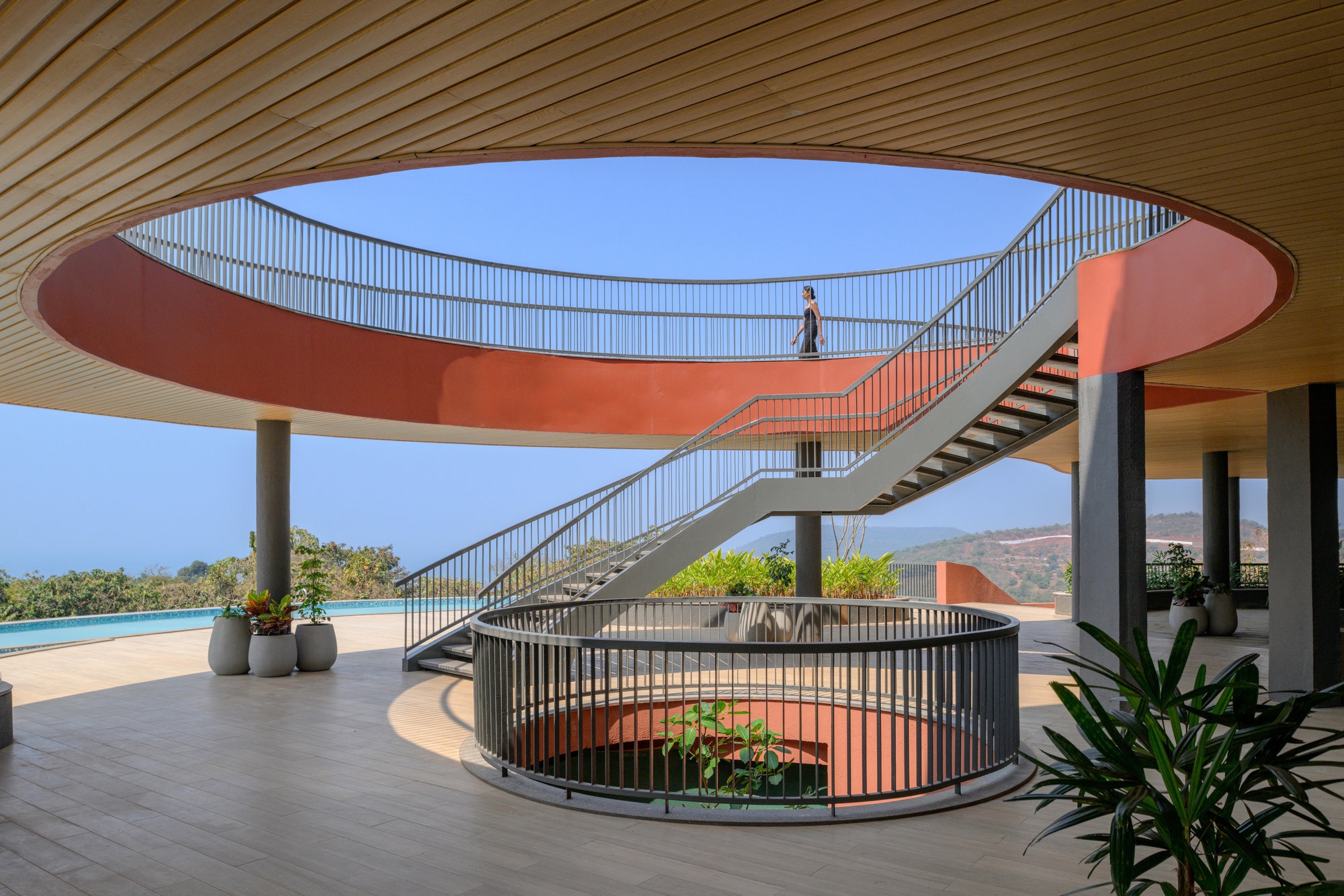 Interior view beneath curved orange bridge linking two levels with spiral staircase and potted plants