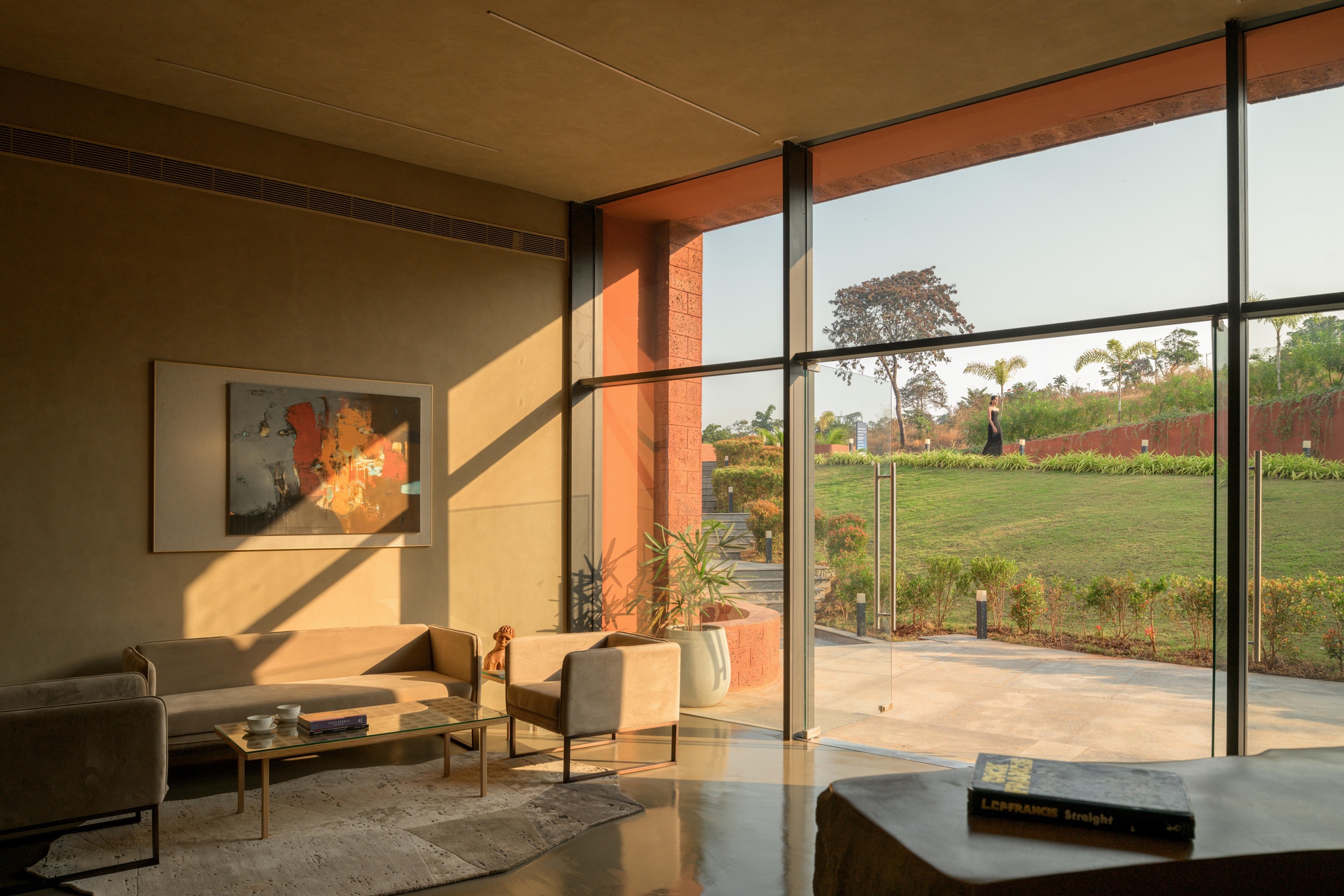 Living area with floor-to-ceiling glass doors framing a planted lawn in warm afternoon sun