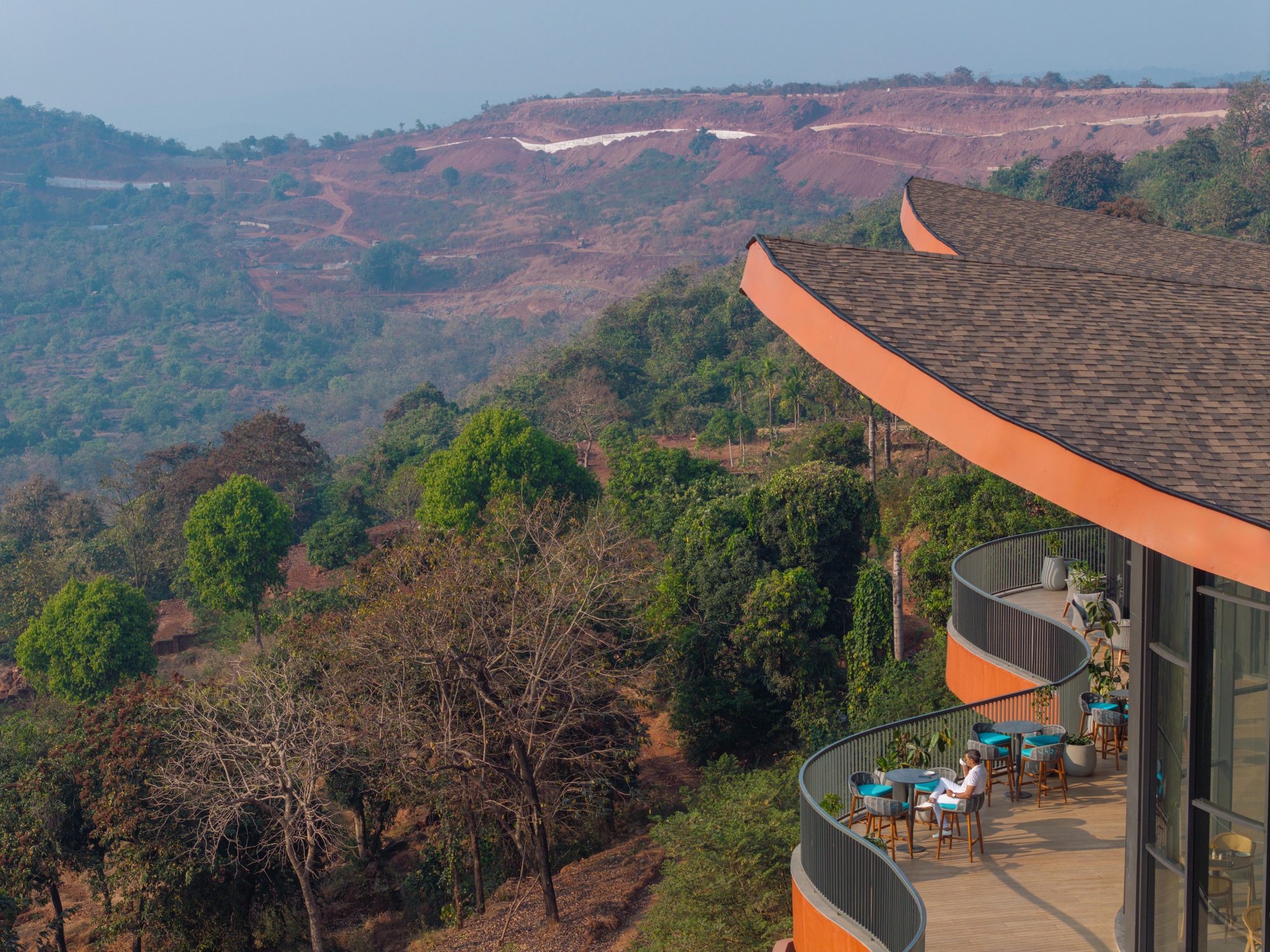 Curved balconies with upturned roof edges extending over a forested hillside landscape