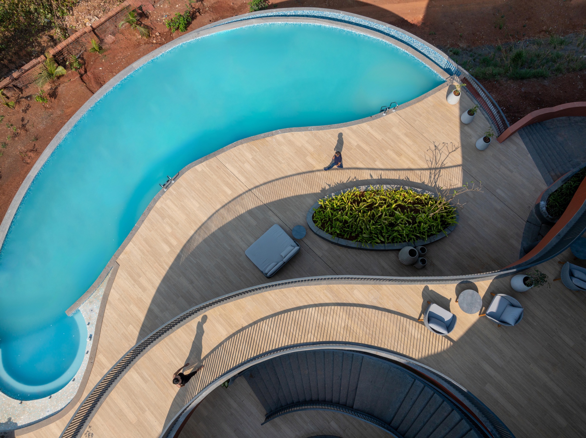 Aerial view of the curved pool deck with planted island and a figure walking