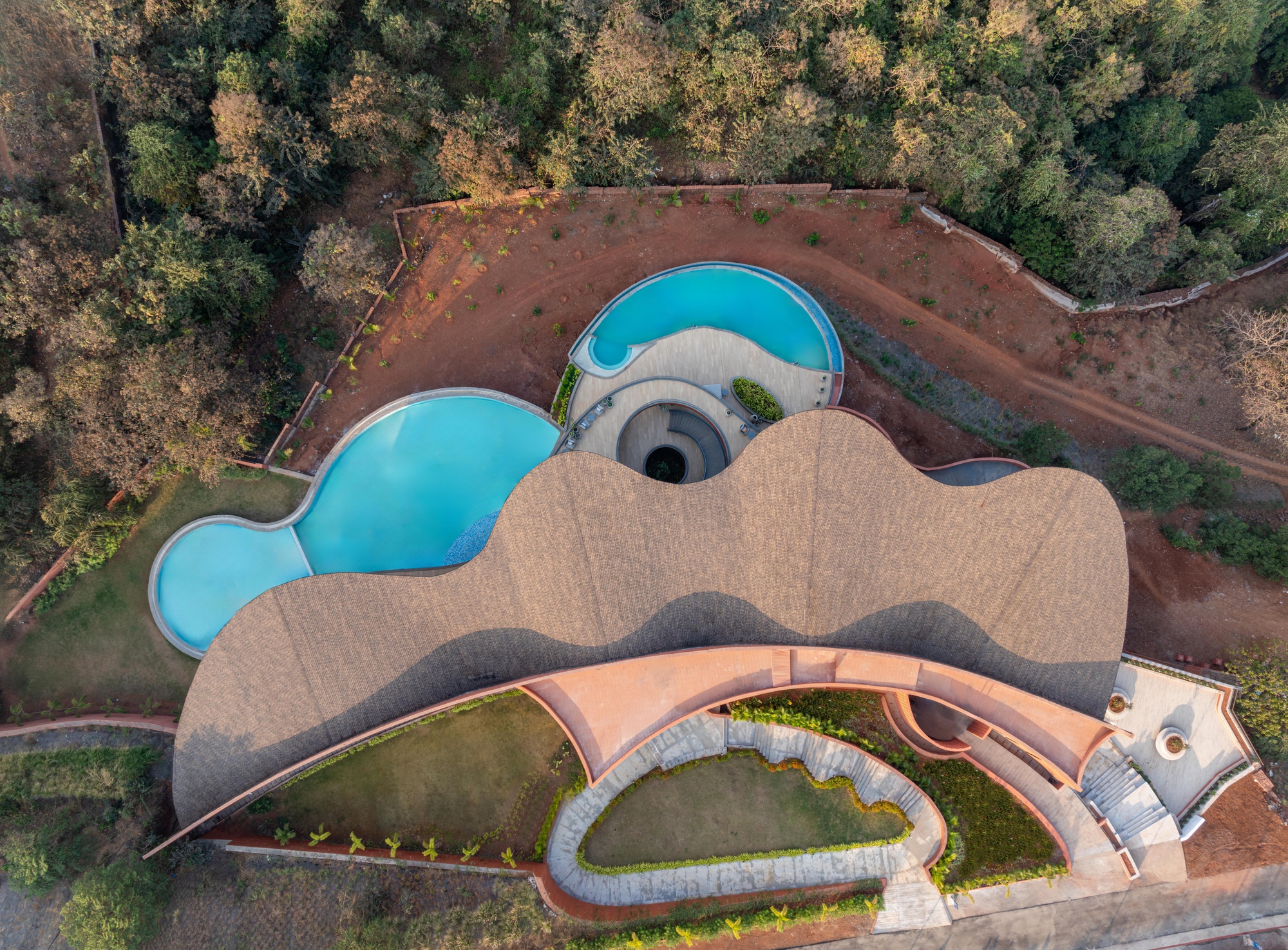 Drone view of the organic roof form with lobed pools and courtyards carved into red earth