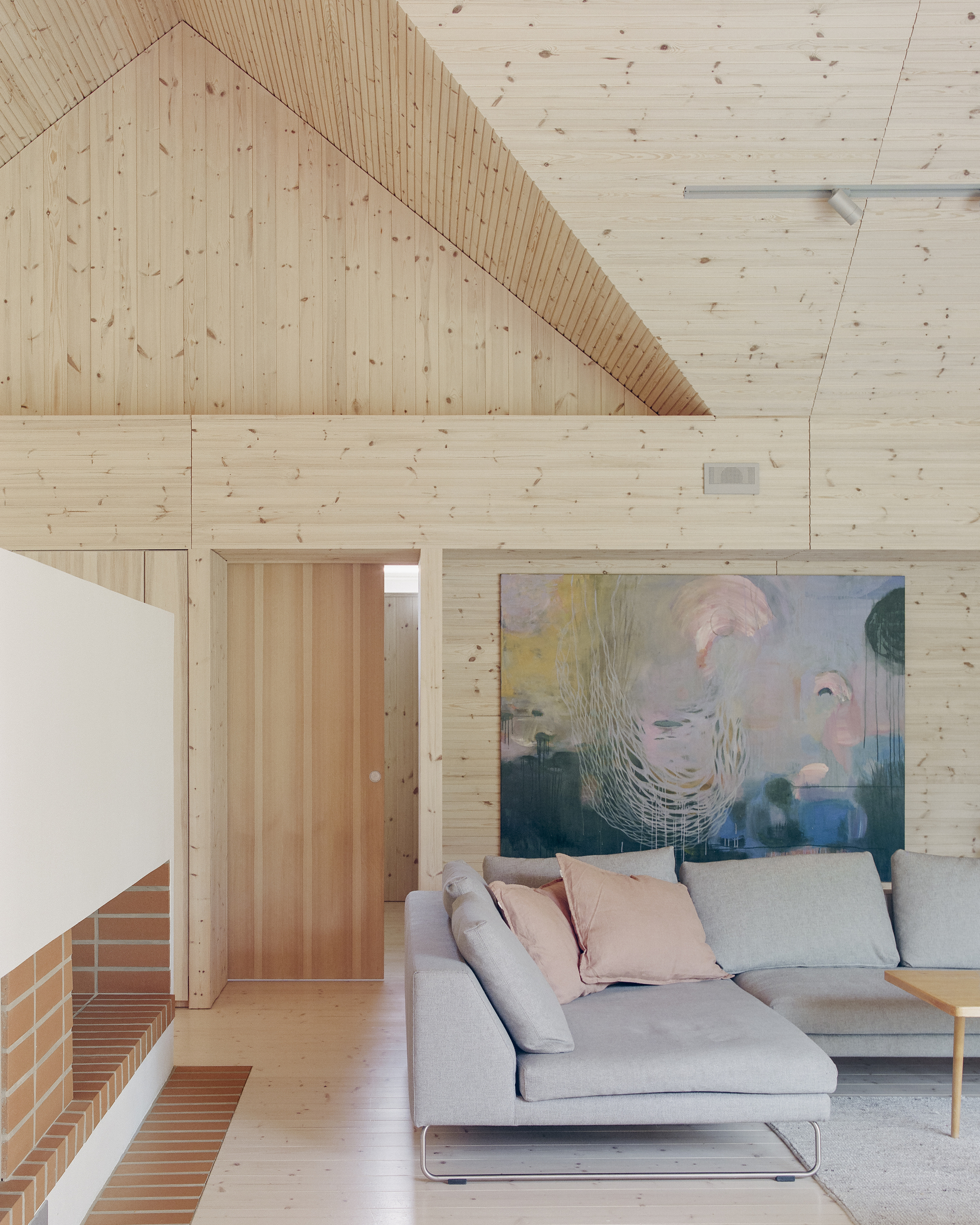 Interior living space with exposed timber plank walls and ceiling above a sofa and brick fireplace surround