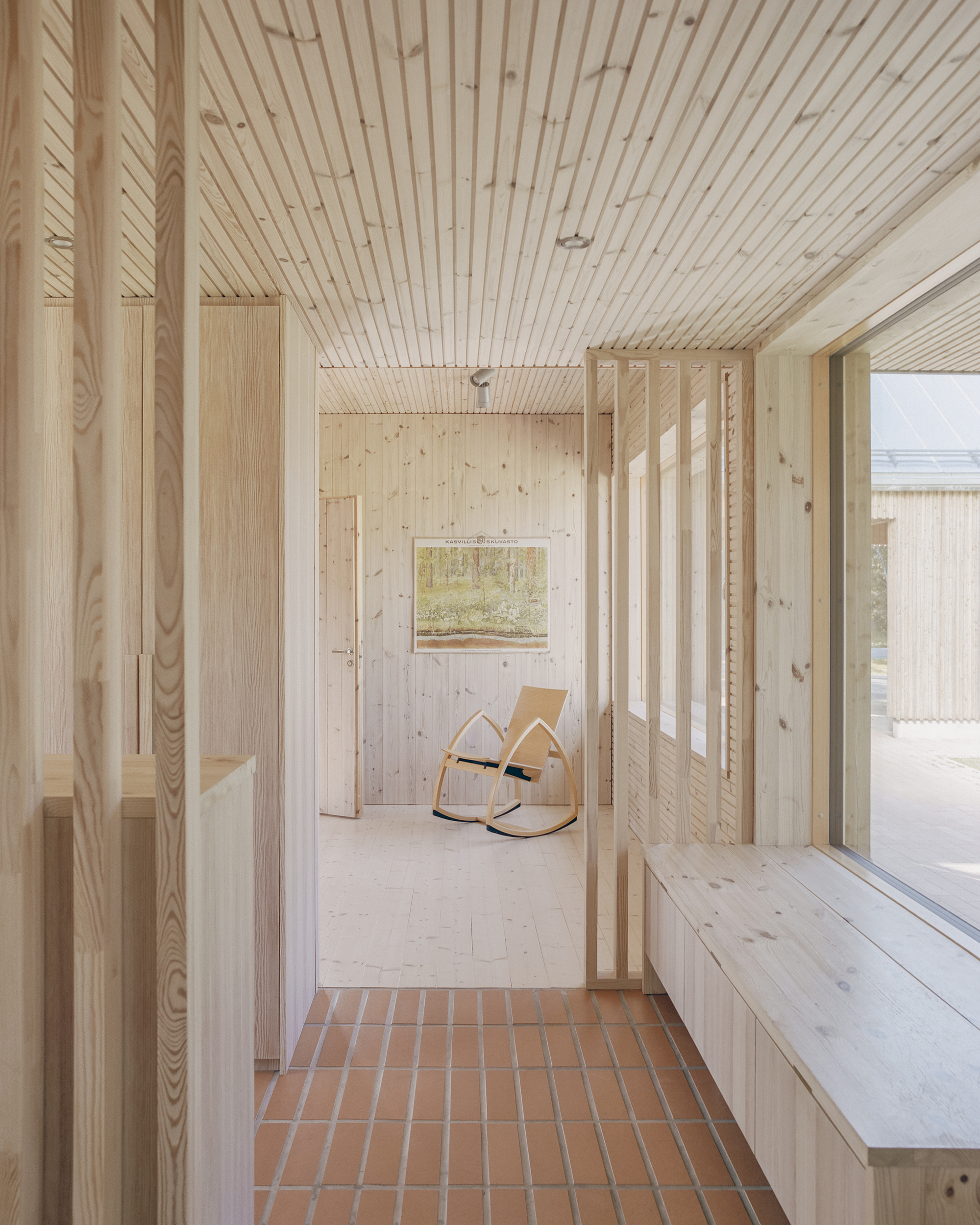 Entry threshold with terracotta tile floor leading to light timber interior with rocking chair and timber slat ceiling