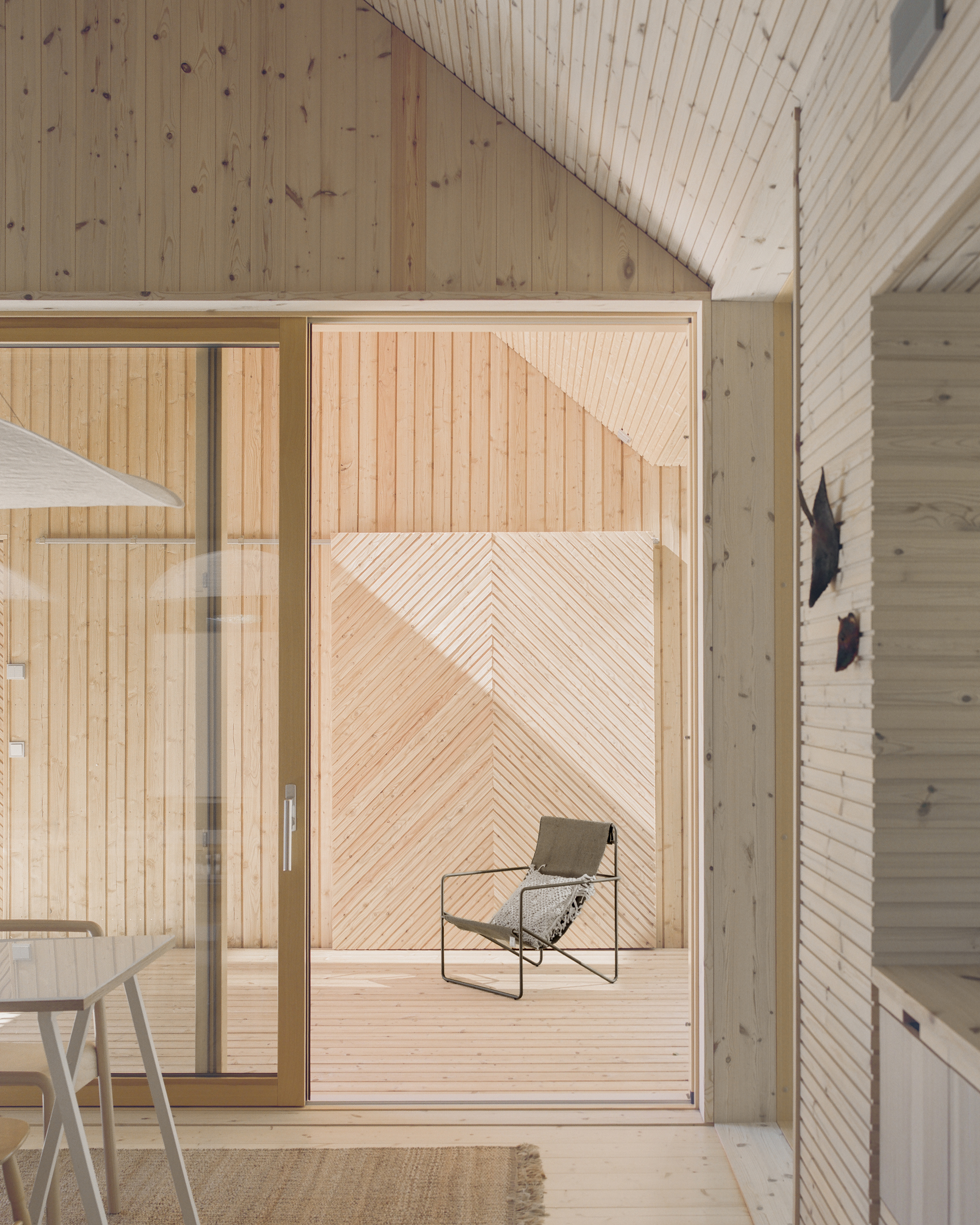 View through sliding glass door to timber deck with lounge chair framed by diagonal wood paneling