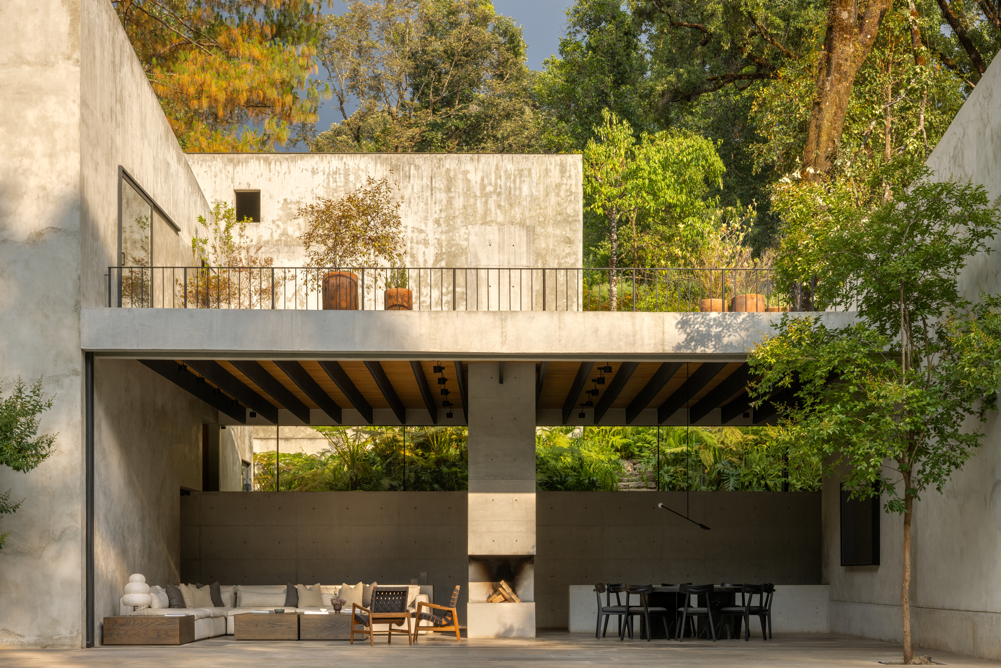 Double-height outdoor terrace with concrete fireplace and exposed beam ceiling beneath upper-level balcony