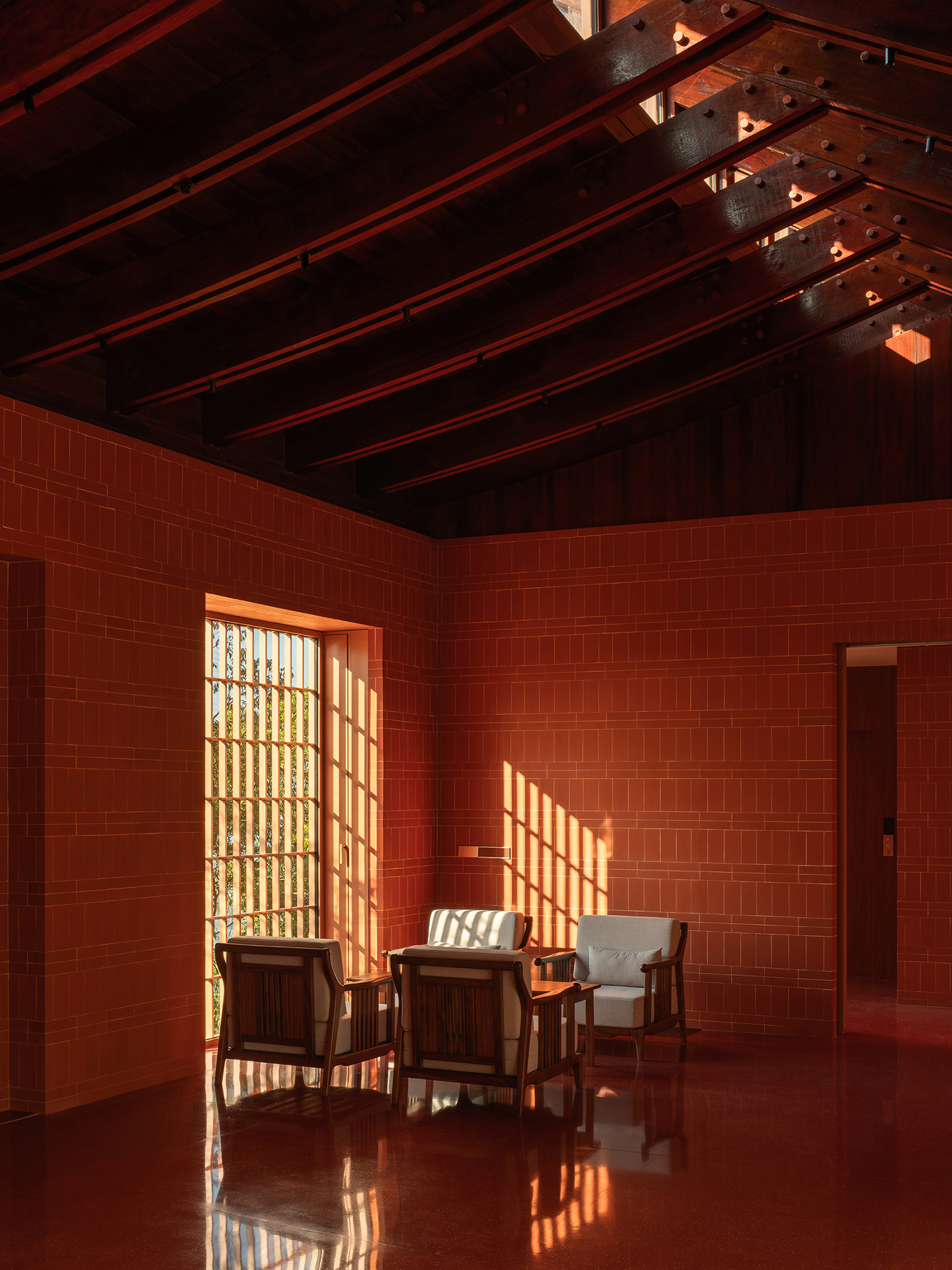Interior room with red tile walls and exposed timber ceiling beams casting patterned light across seating