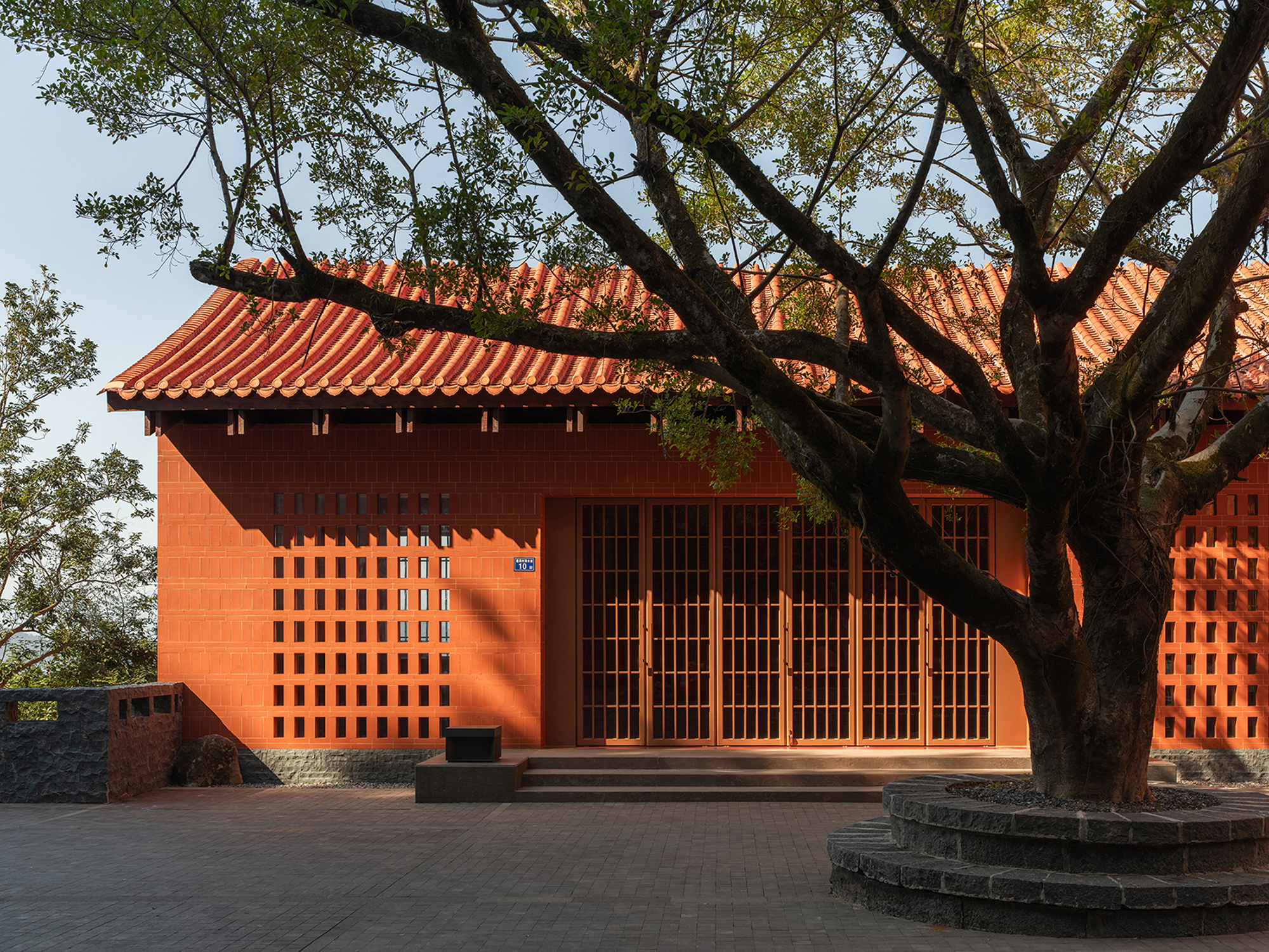 Front facade with latticed red tile screen and terracotta roof beneath overhanging tree branches
